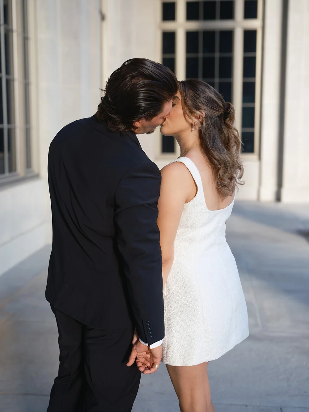 Groom and bride kissing on the courthouse walkway between the stone columns