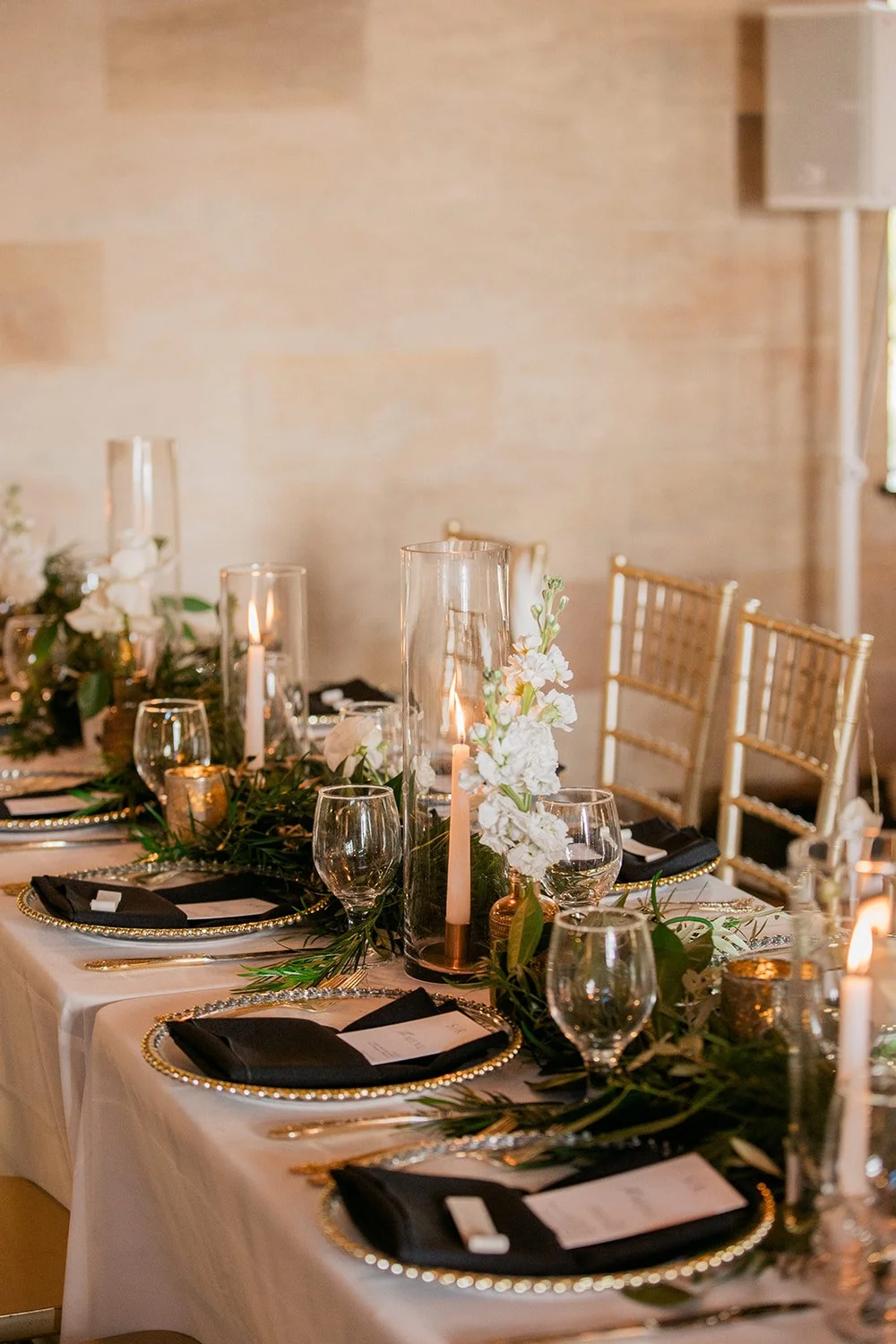 Long reception table inside the Powel Crosley Estate set with candles, greenery, gold chairs and black napkins