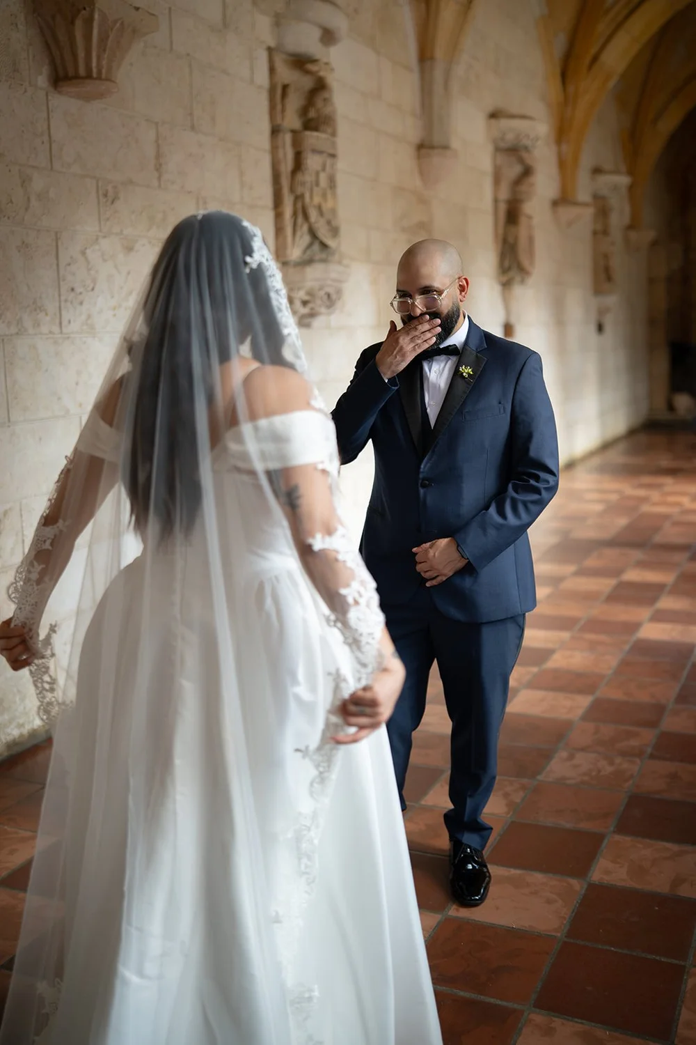 Christian laughing with a hand at his face as Maria stands in front of him in the cloister