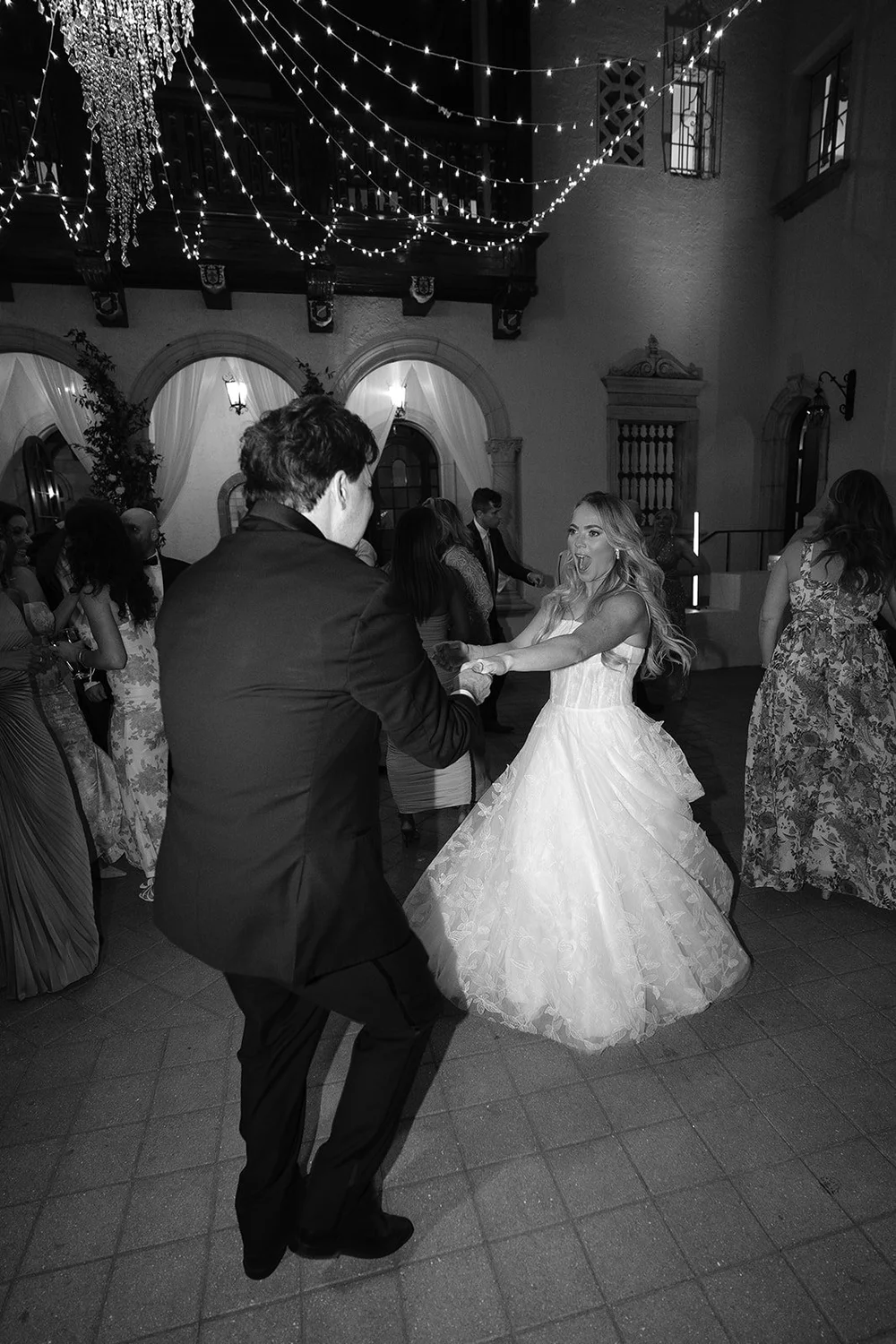 Black and white photo of Jane dancing with a guest under the string lights in the Powel Crosley Estate courtyard