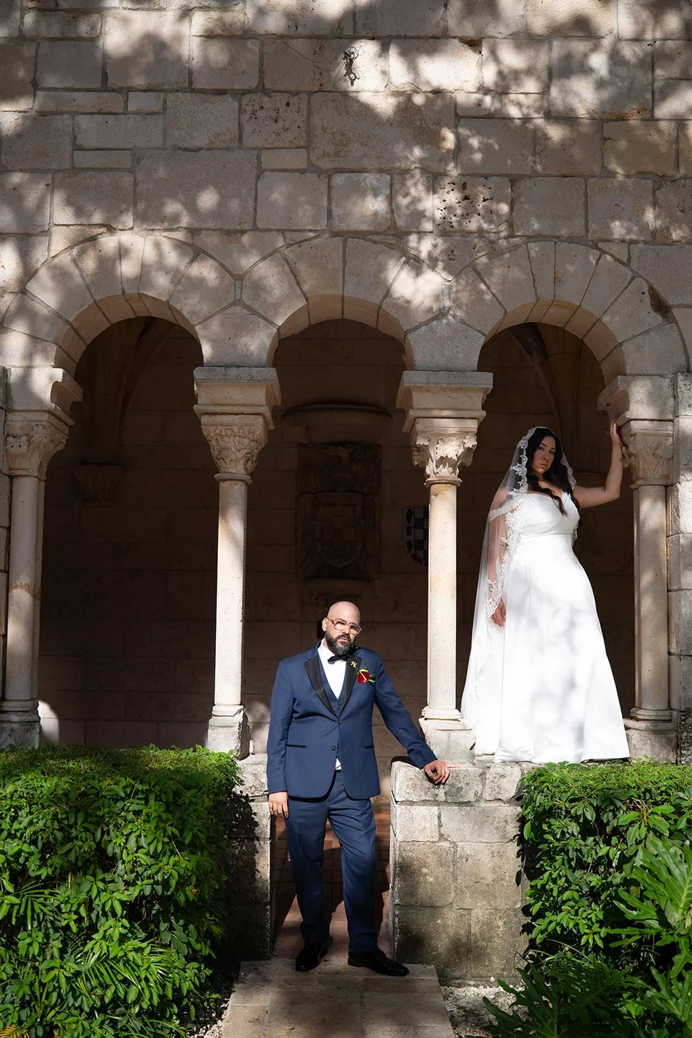 Christian leaning on a stone wall while Maria stands in a stone archway behind him