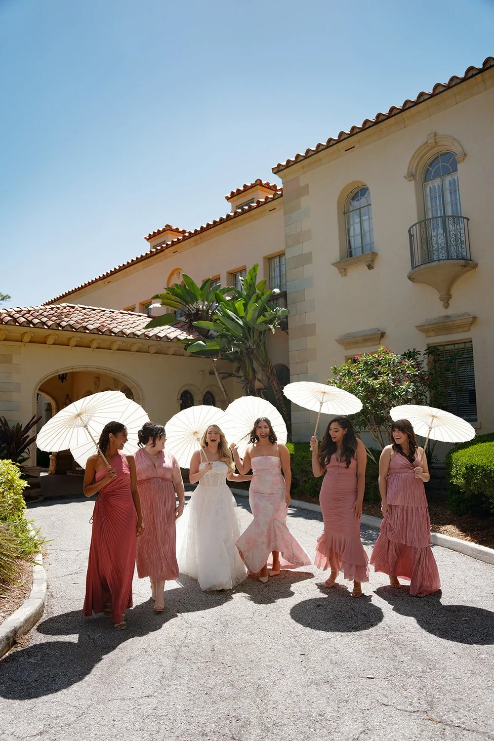 Jane and her bridesmaids in dusty rose dresses holding white parasols in the courtyard of the estate