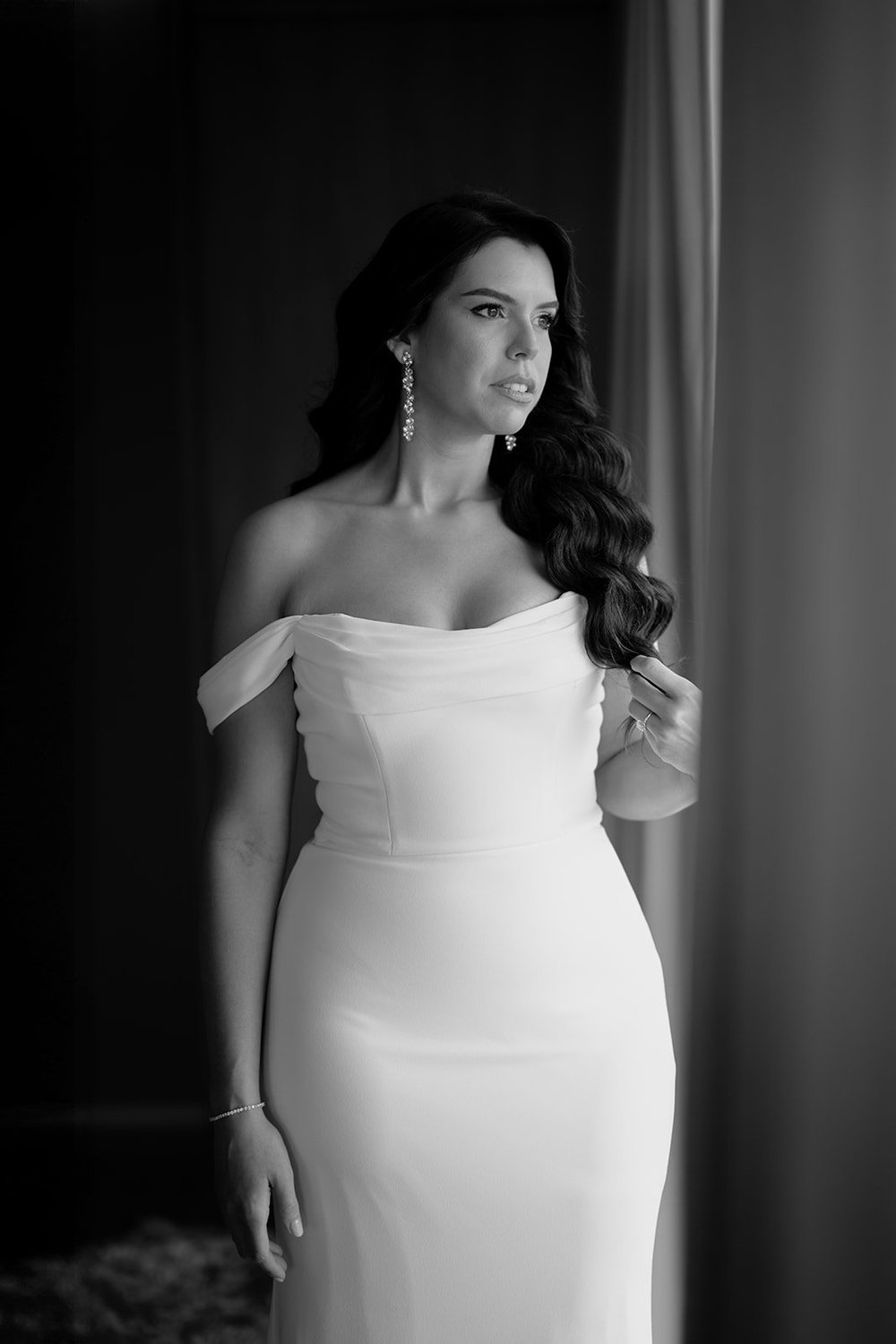 Black and white portrait of Krystine standing beside a curtained window in her wedding gown