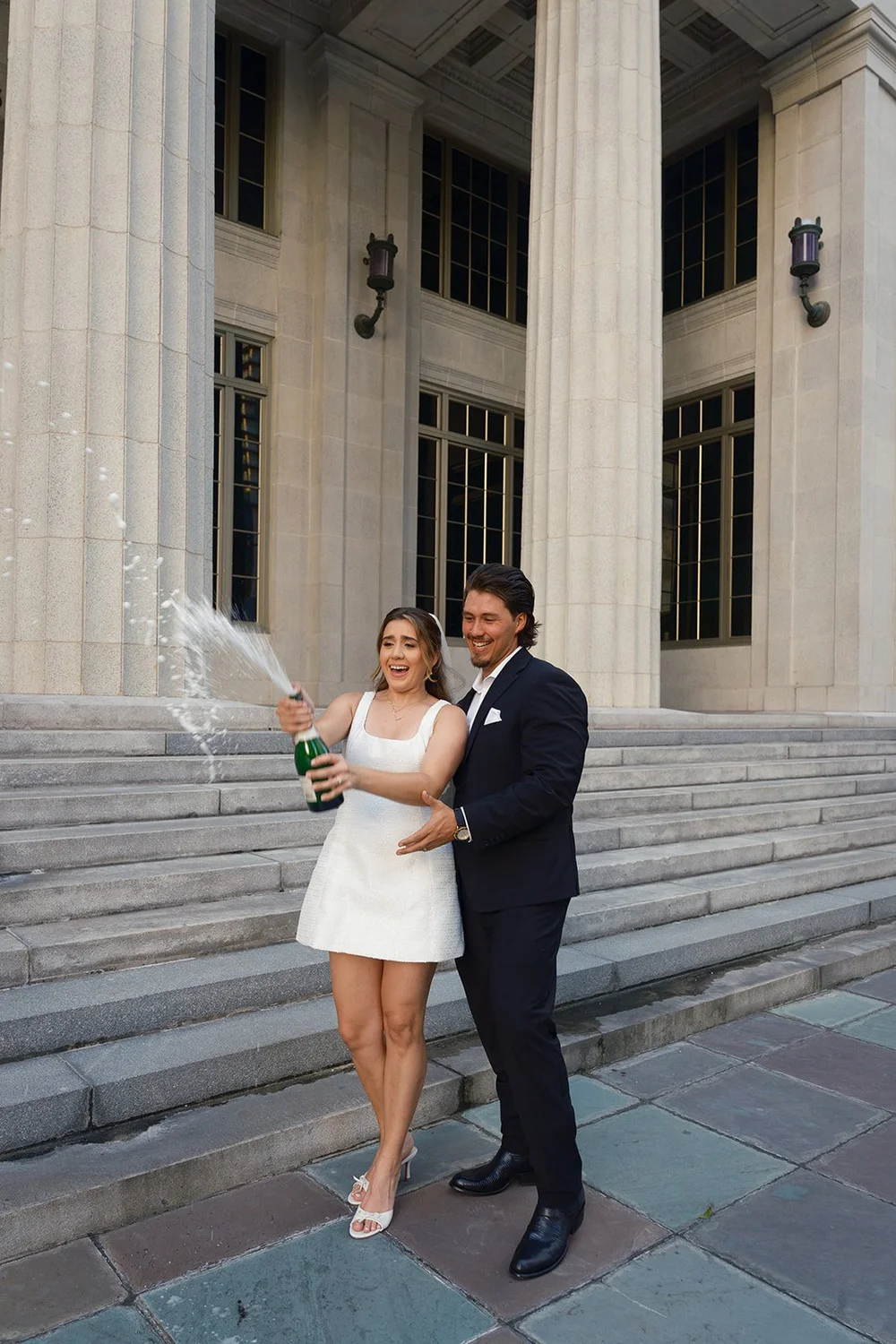 Bride and groom standing on the courthouse steps as a bottle sprays beside them