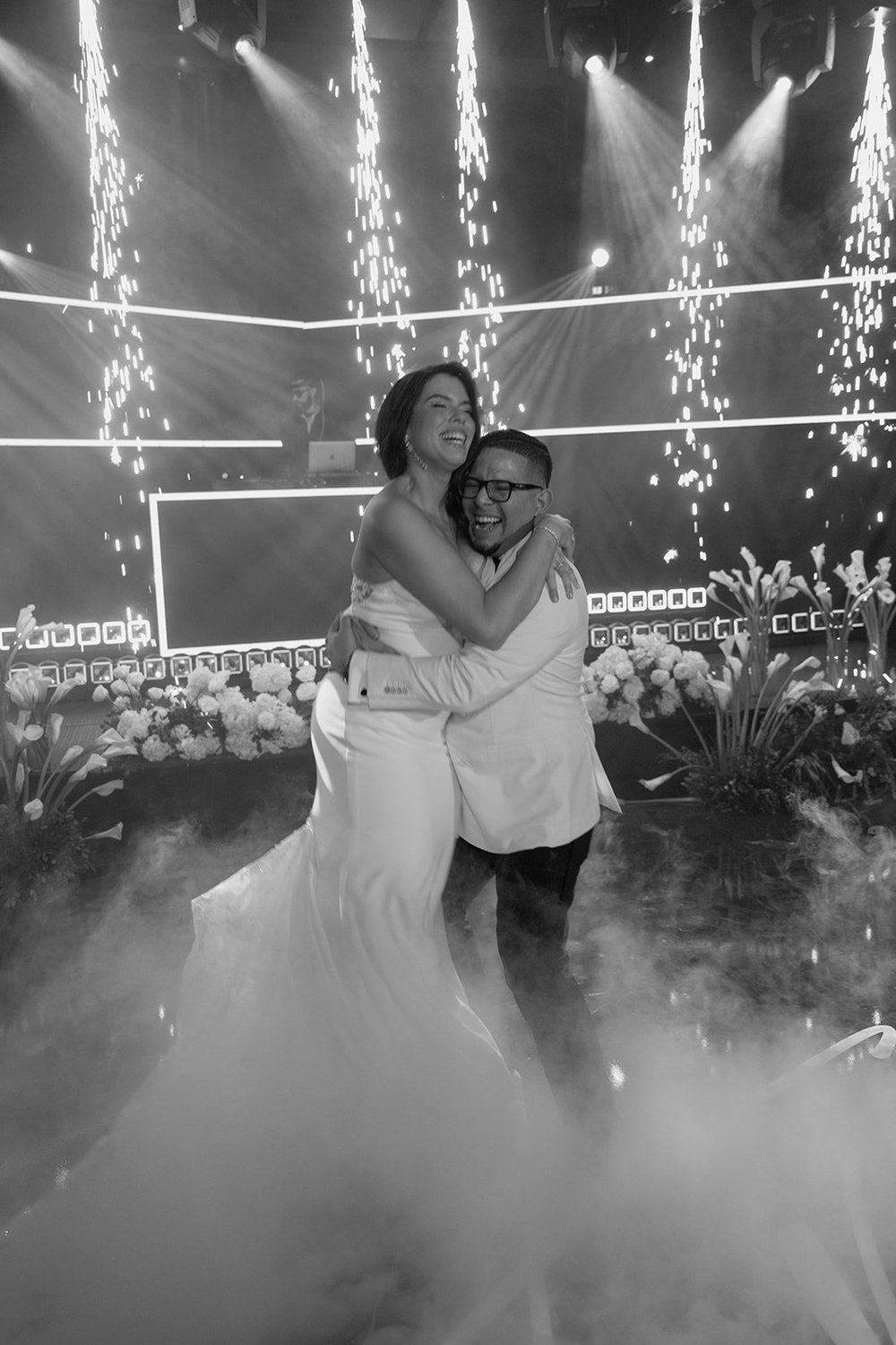 Black and white photo of Krystine and Douglas embracing as they dance in low fog with sparks behind them