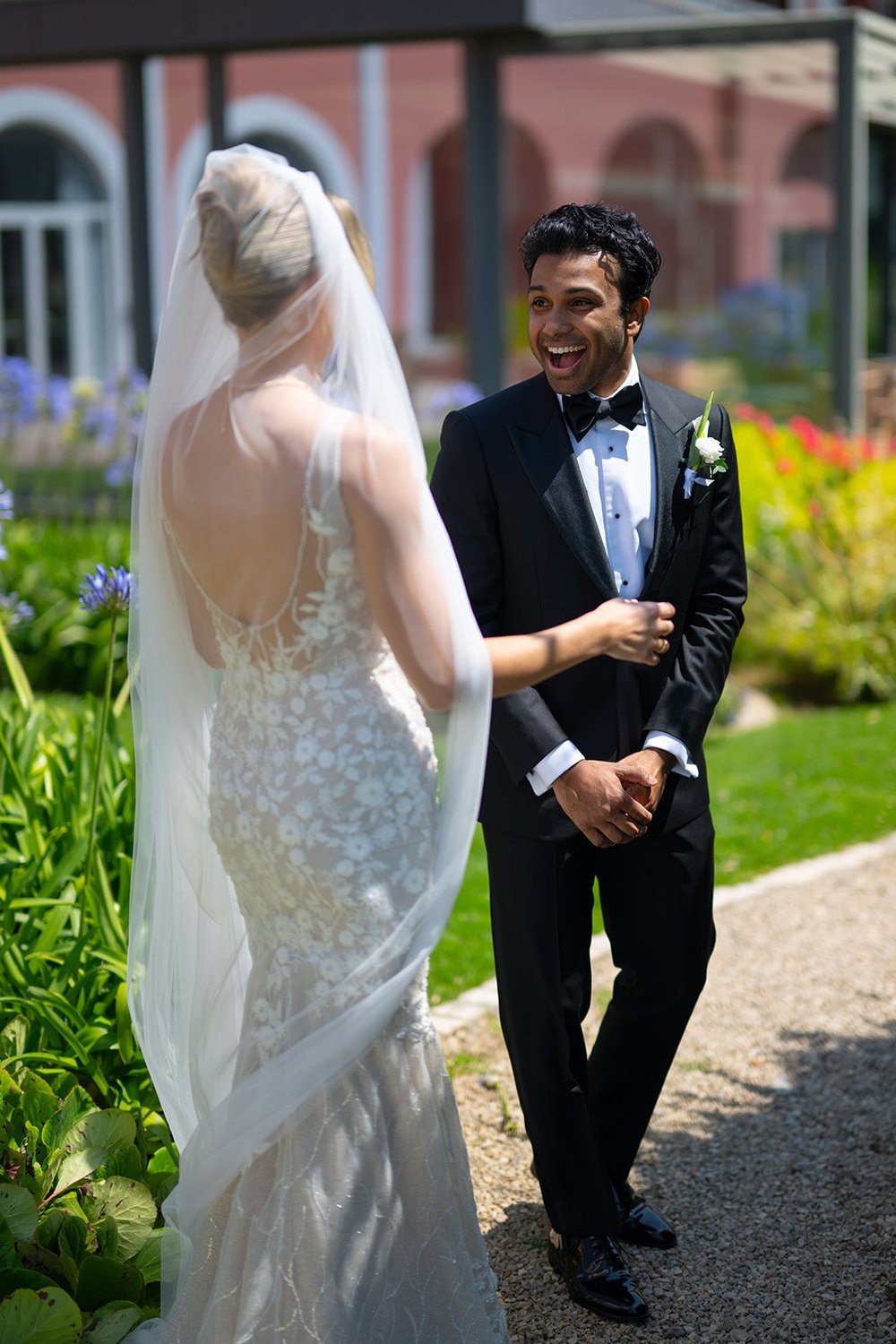 Ellen in her veil and beaded dress beside Jacob on a garden path with pink buildings behind them