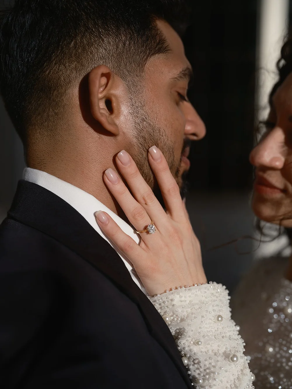 Close portrait of the bride's hand with a ring resting on the groom's cheek