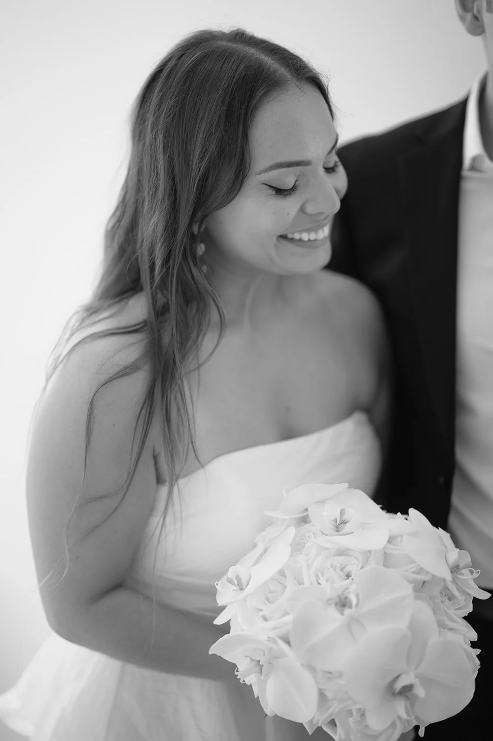Black and white profile of Chris smiling down at her bouquet of white roses