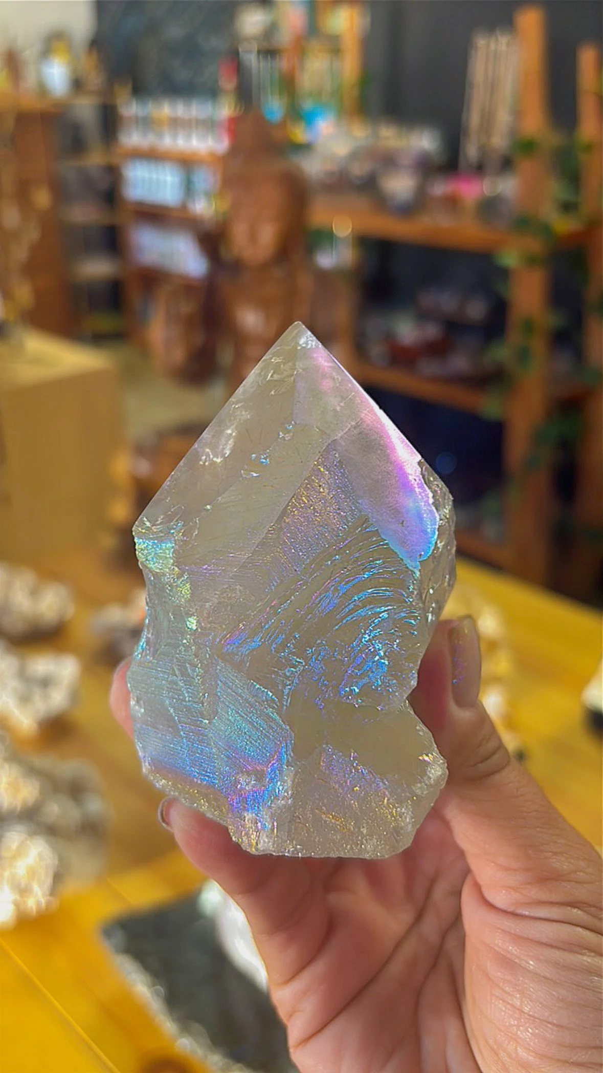 Angel Aura Quartz point with shimmering rainbow surface, held in hand inside Soul II Soul store.