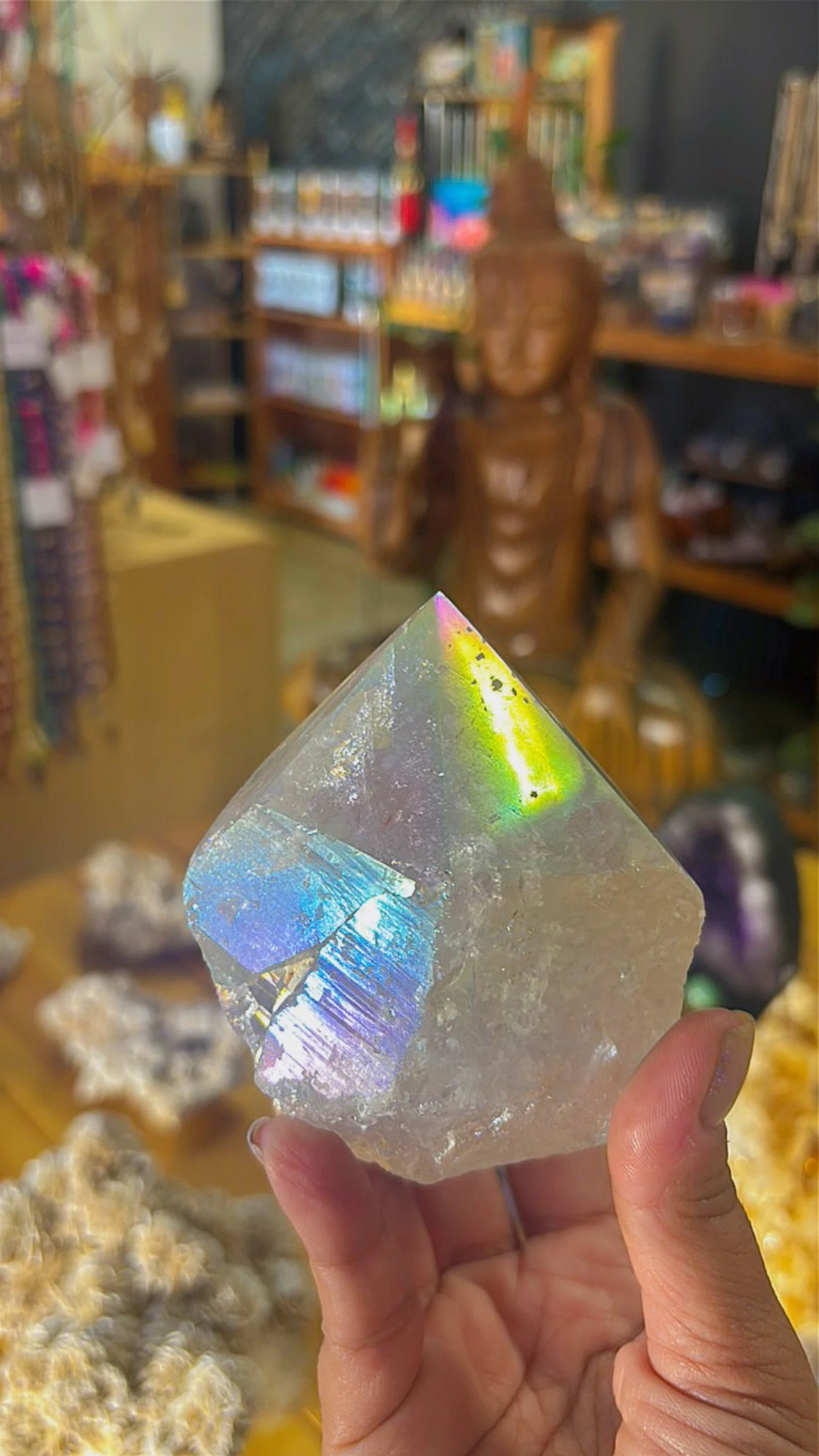 Angel Aura Quartz point with shimmering rainbow surface, held in hand inside Soul II Soul store.