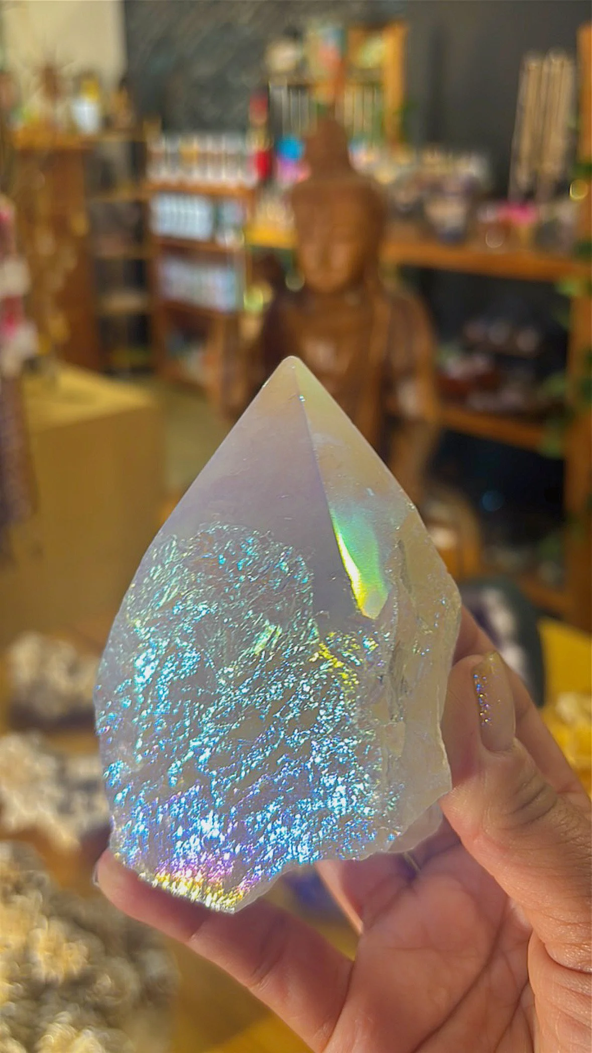 Angel Aura Quartz point with shimmering rainbow surface, held in hand inside Soul II Soul store.