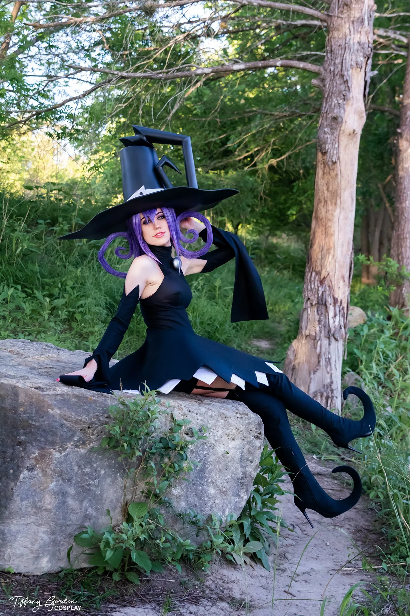 Blair from Soul Eater cosplay by Tiffany Gordon Cosplay, featuring an oversized hat with curly purple hair, a black mini dress with white ruffles, and yellow cat-eye contacts.