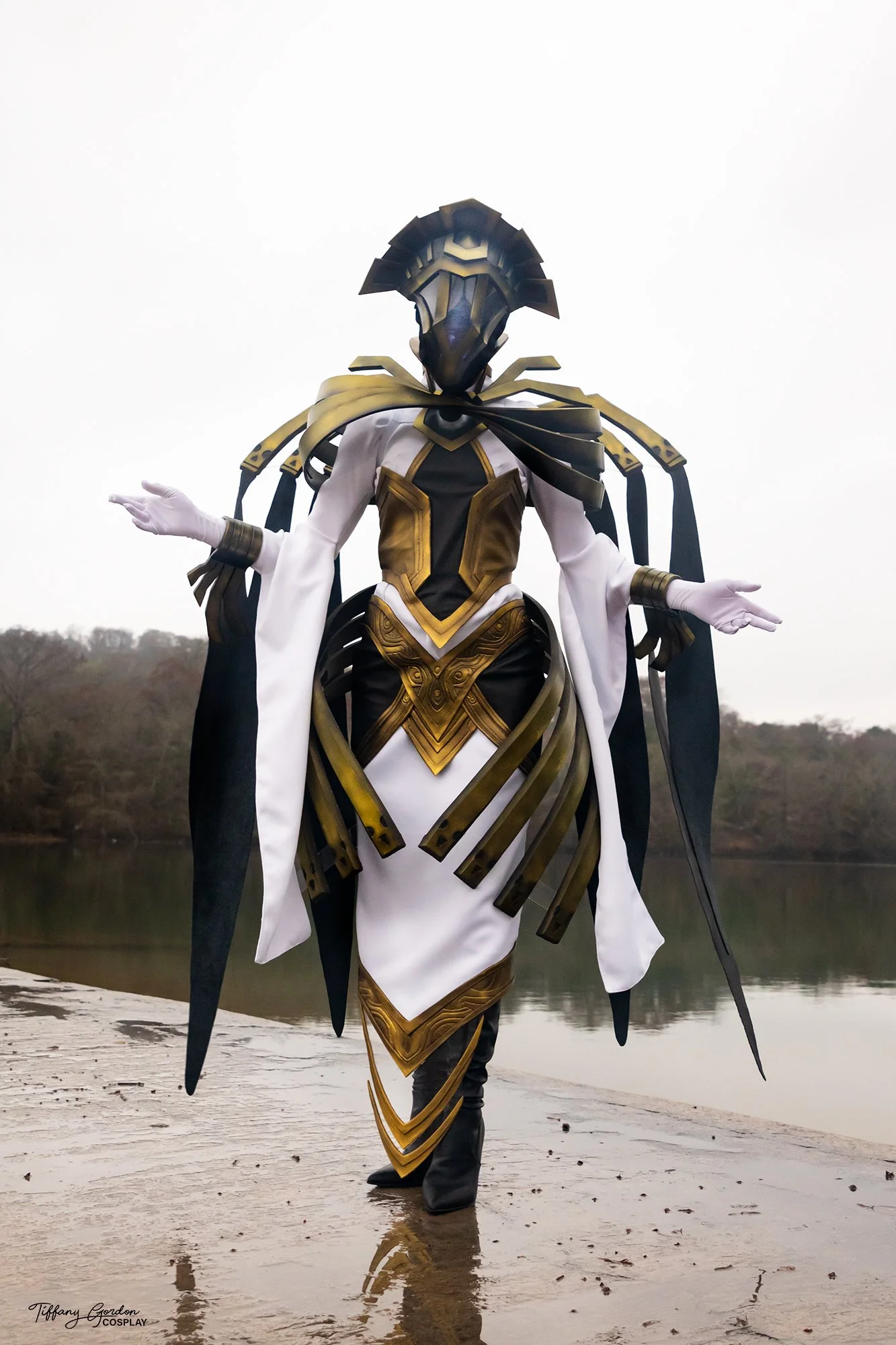 The Arbiter cosplay from World of Warcraft by Tiffany Gordon Cosplay, featuring polished gold mechanical armor, a glowing orb in the chest, and floating gold halo structures.
