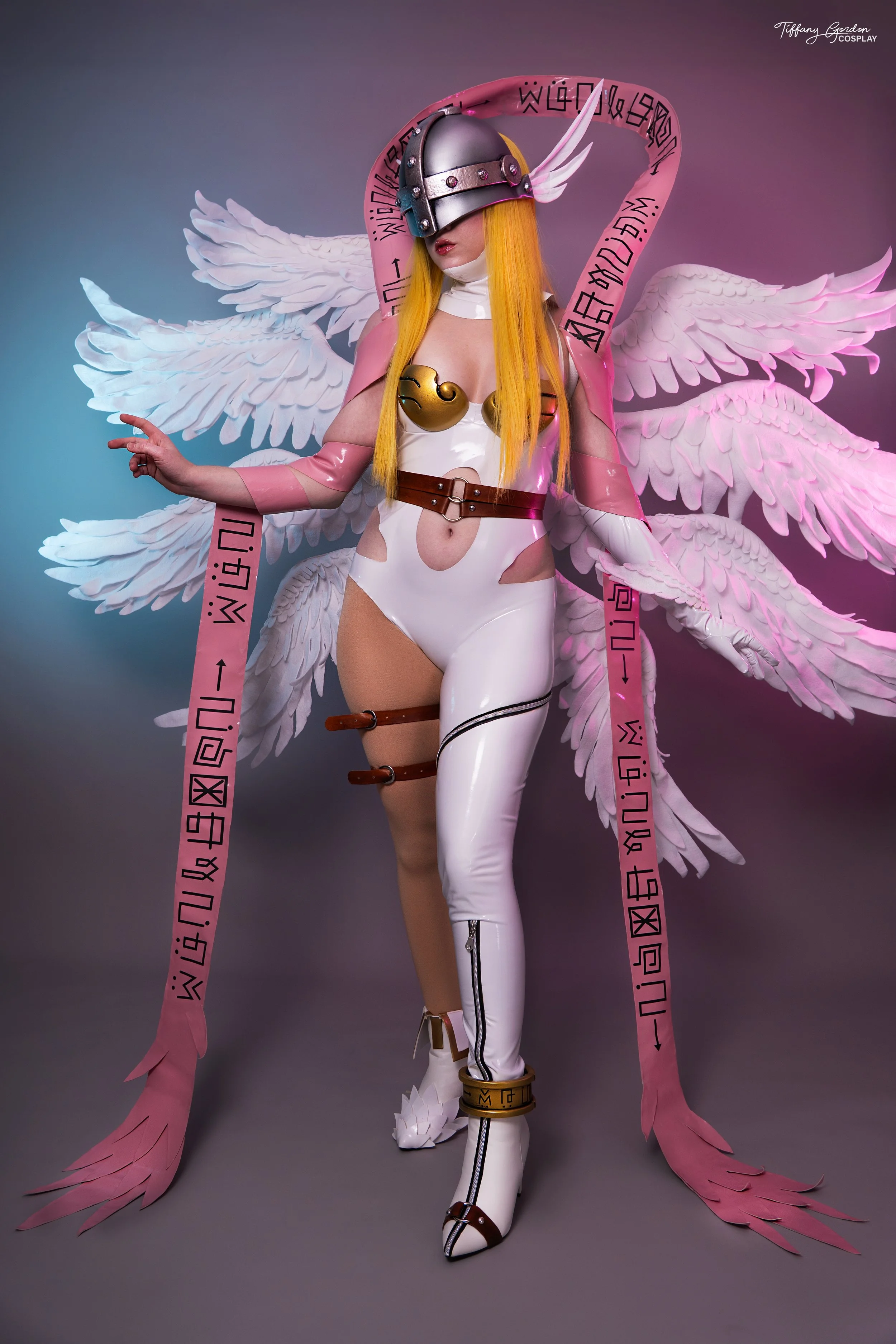 Angewomon cosplay from Digimon by Tiffany Gordon Cosplay, featuring eight large white feathered wings, a pink Holy Ribbon with digital runes, a silver winged helmet, and a white bodysuit.