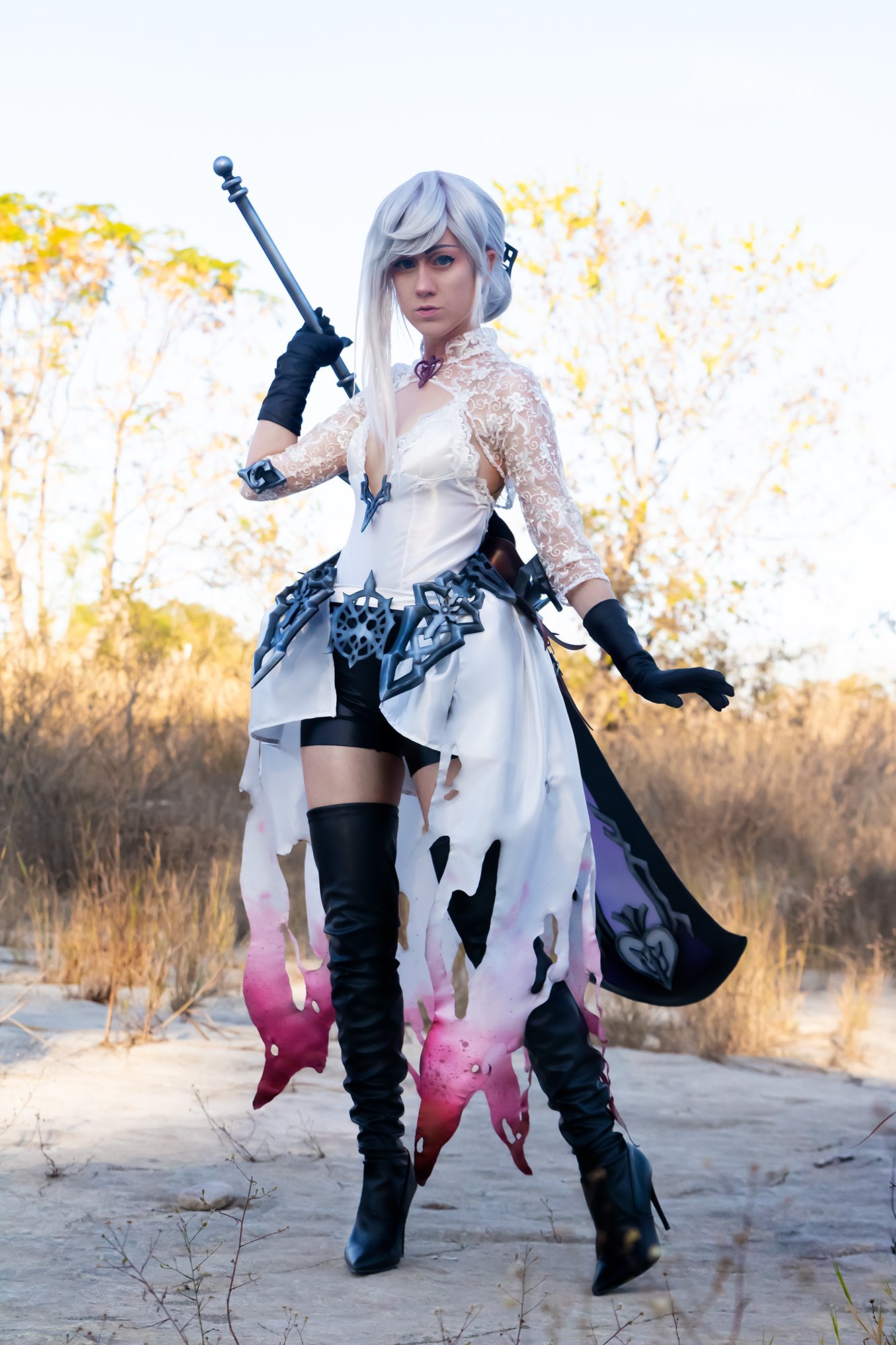 Snow White cosplay from SINoALICE by Tiffany Gordon Cosplay, featuring a lace bodice, tattered white and pink skirt, black thigh-high boots, and a large staff in an outdoor field.