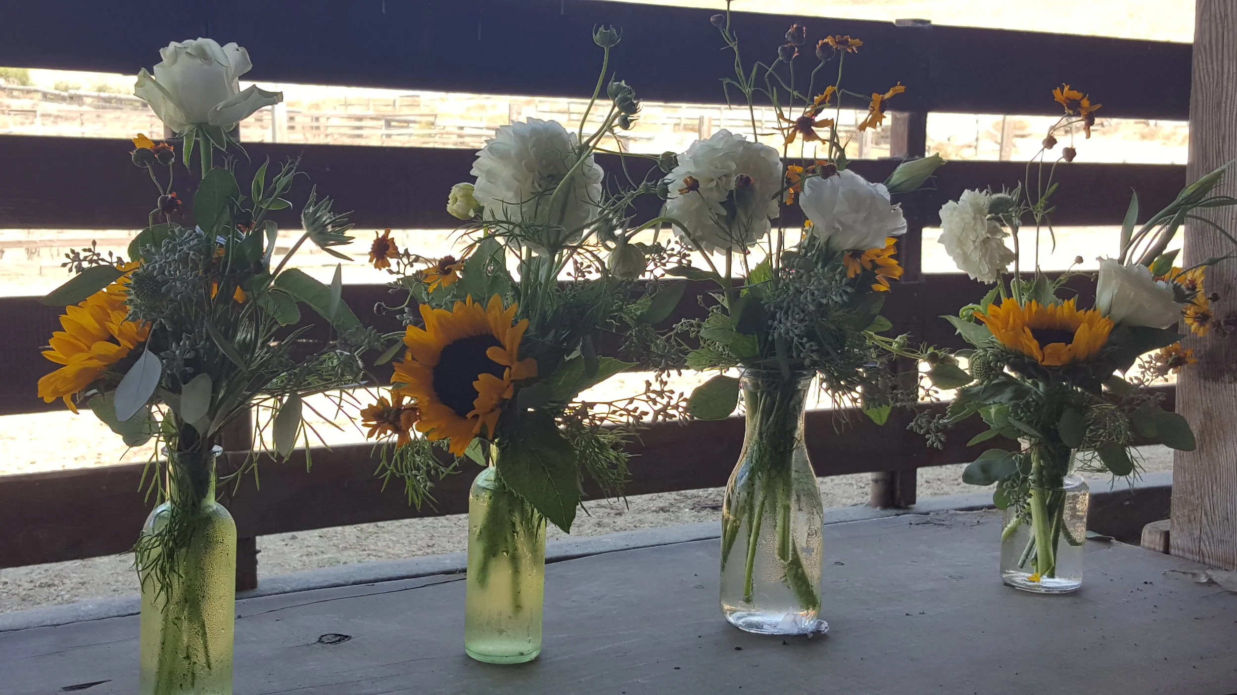 Milk bottle vases with local wild flowers line farm tables for rustic barn wedding centerpiece flowers.