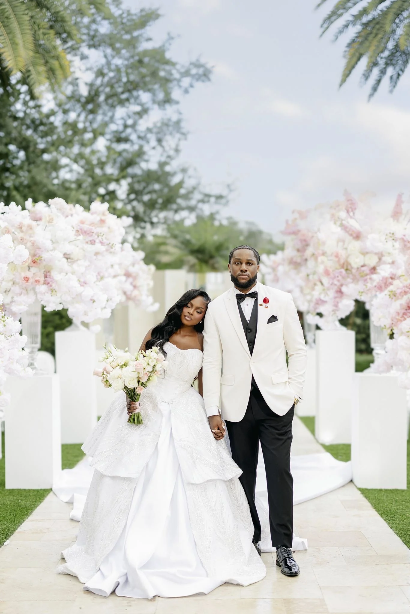 Bride and groom walking together beside pink and white wedding florals, photographed by Topflash Photography