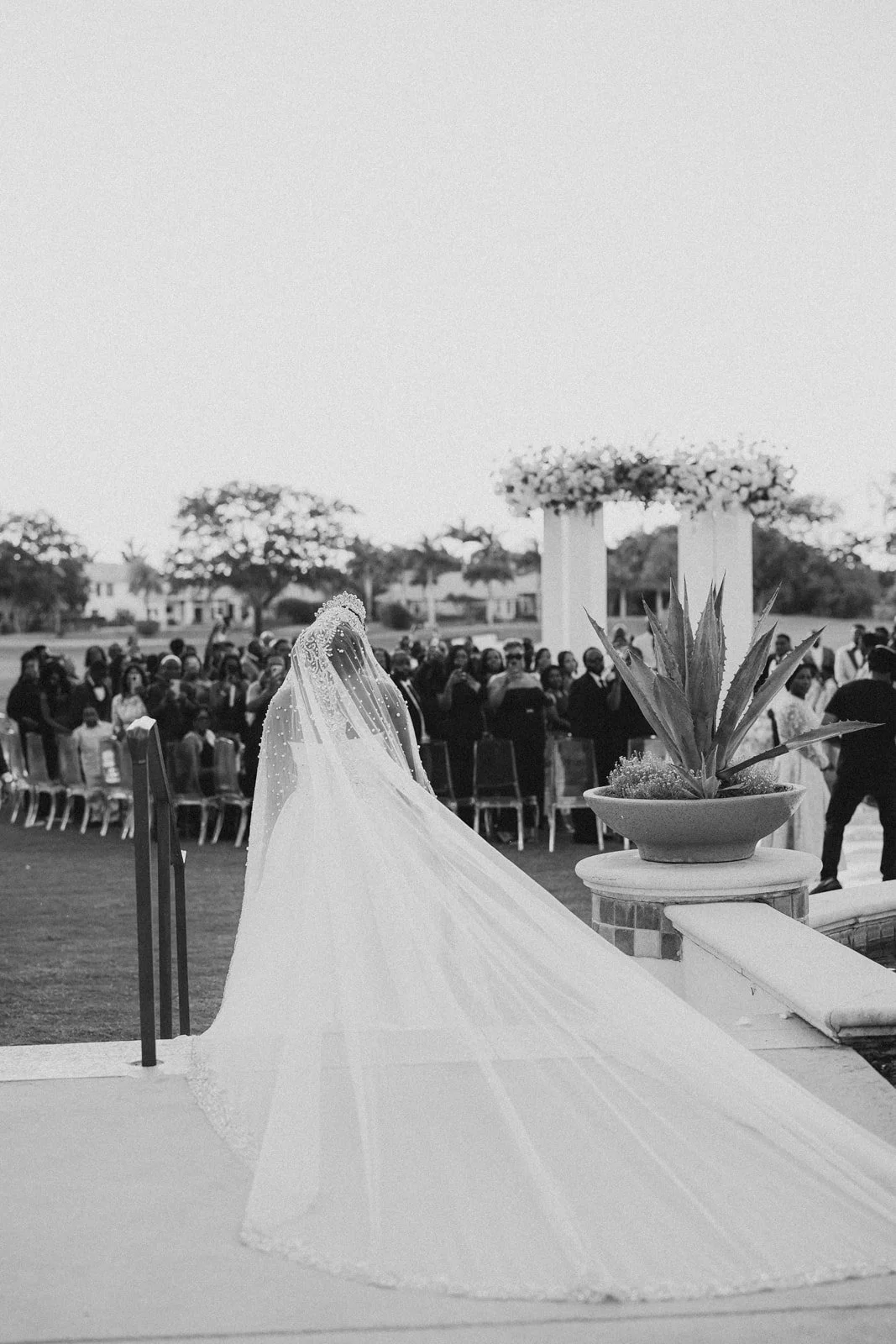 Bride in a long cathedral veil walking toward an outdoor ceremony, photographed by Topflash Photography