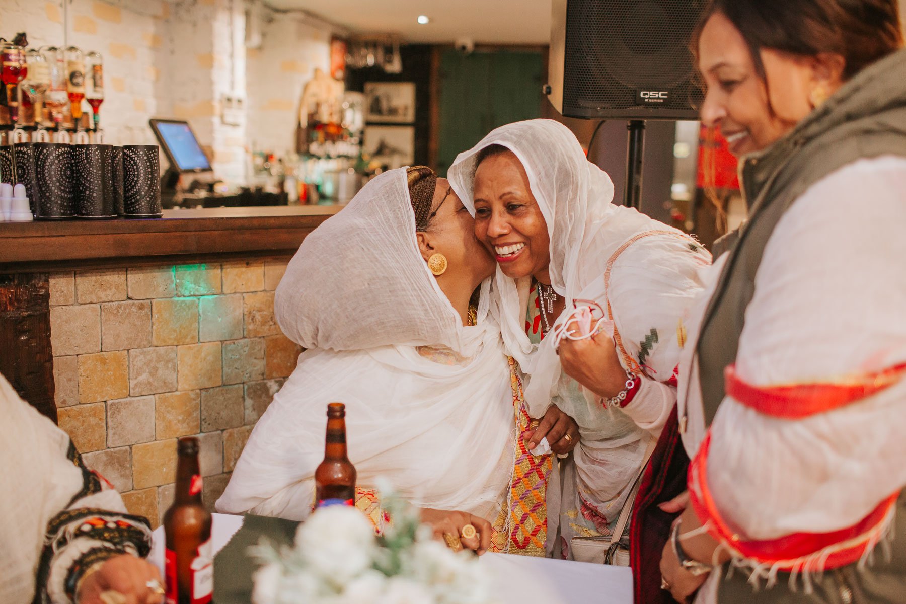 Guests of the Christening embracing each other and dressed in traditional Eritrean dress.