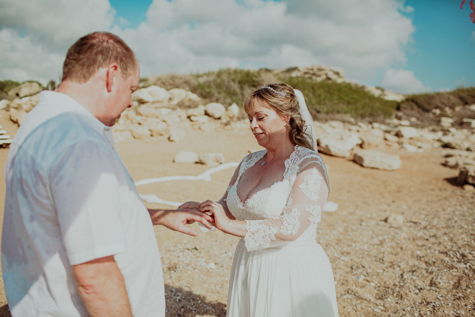 Groom putting ring on bride on St Georges beach peyia paphos