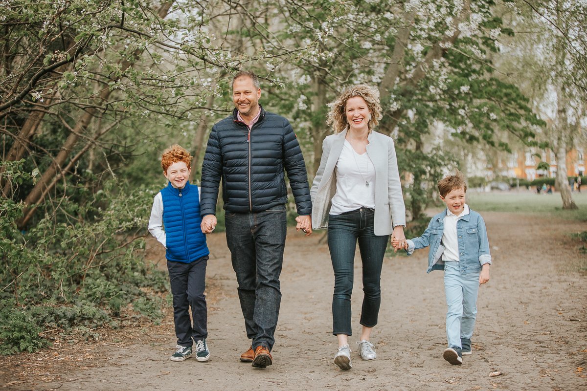  Family of mum dad and two boys holding hands and walking through Tooting Common. 