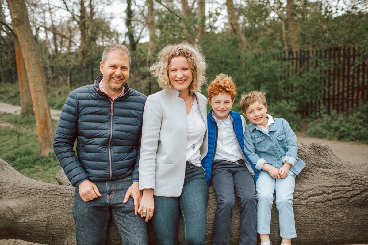 Mum, Dad and their two boys sitting on a log in Tooting Commons.