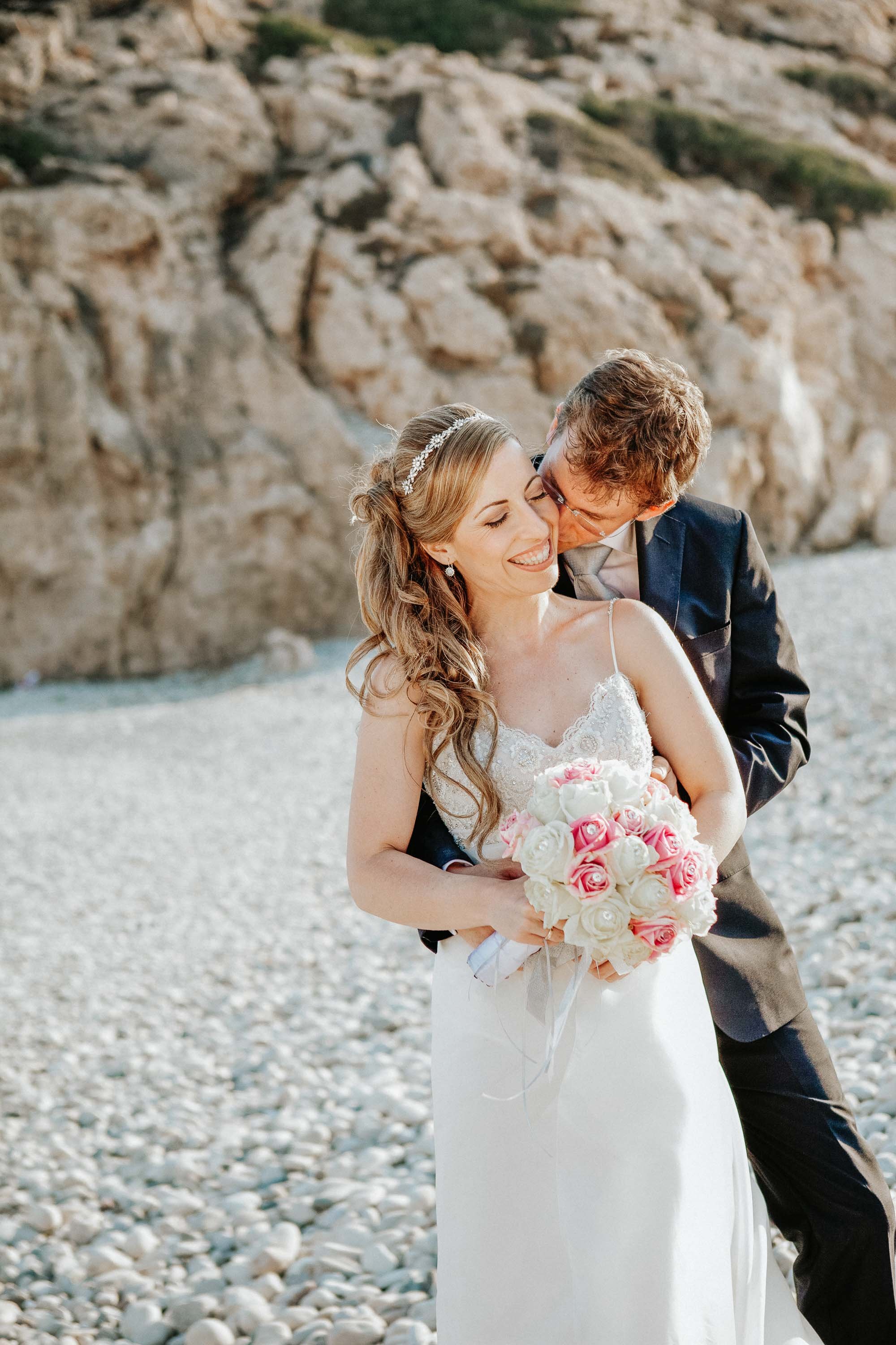 Married couple kissing other by Aphrodites Rock (Petra tou Romiou) Cyprus.