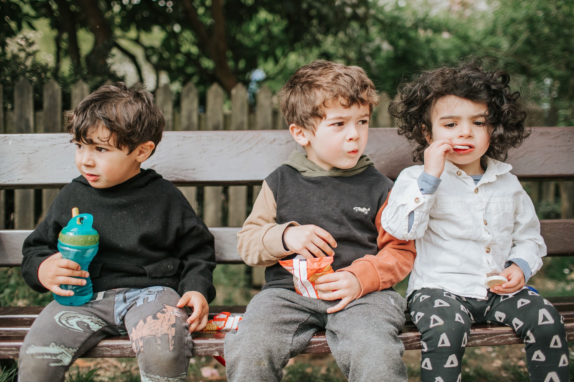 Three boys sitting on the bench eating in Highgate Woods.