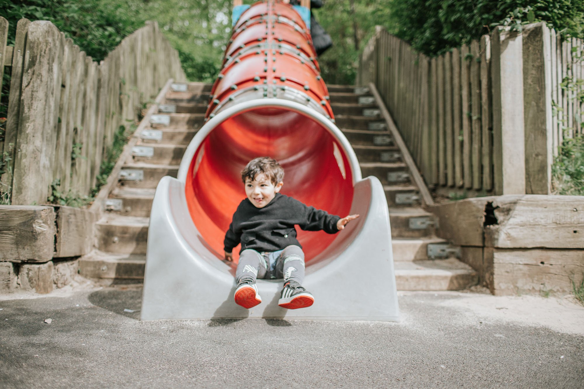 Young boy coming out of tube slide in playground highgate woods.