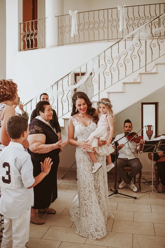 Bride walks in to her stolisma with musician playing violin in the background.