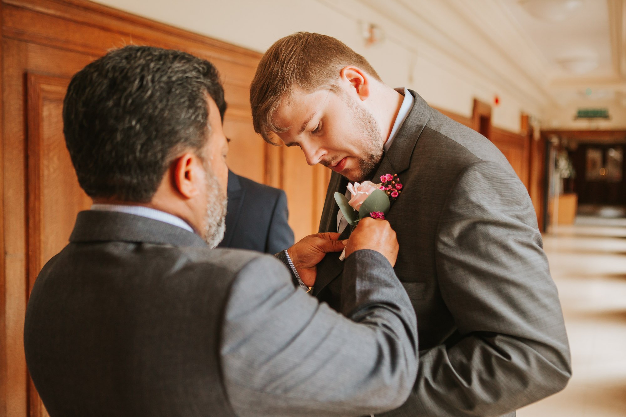  Groom having his button hole filled with a flower at his wedding in Wandsworth Town Hall. 