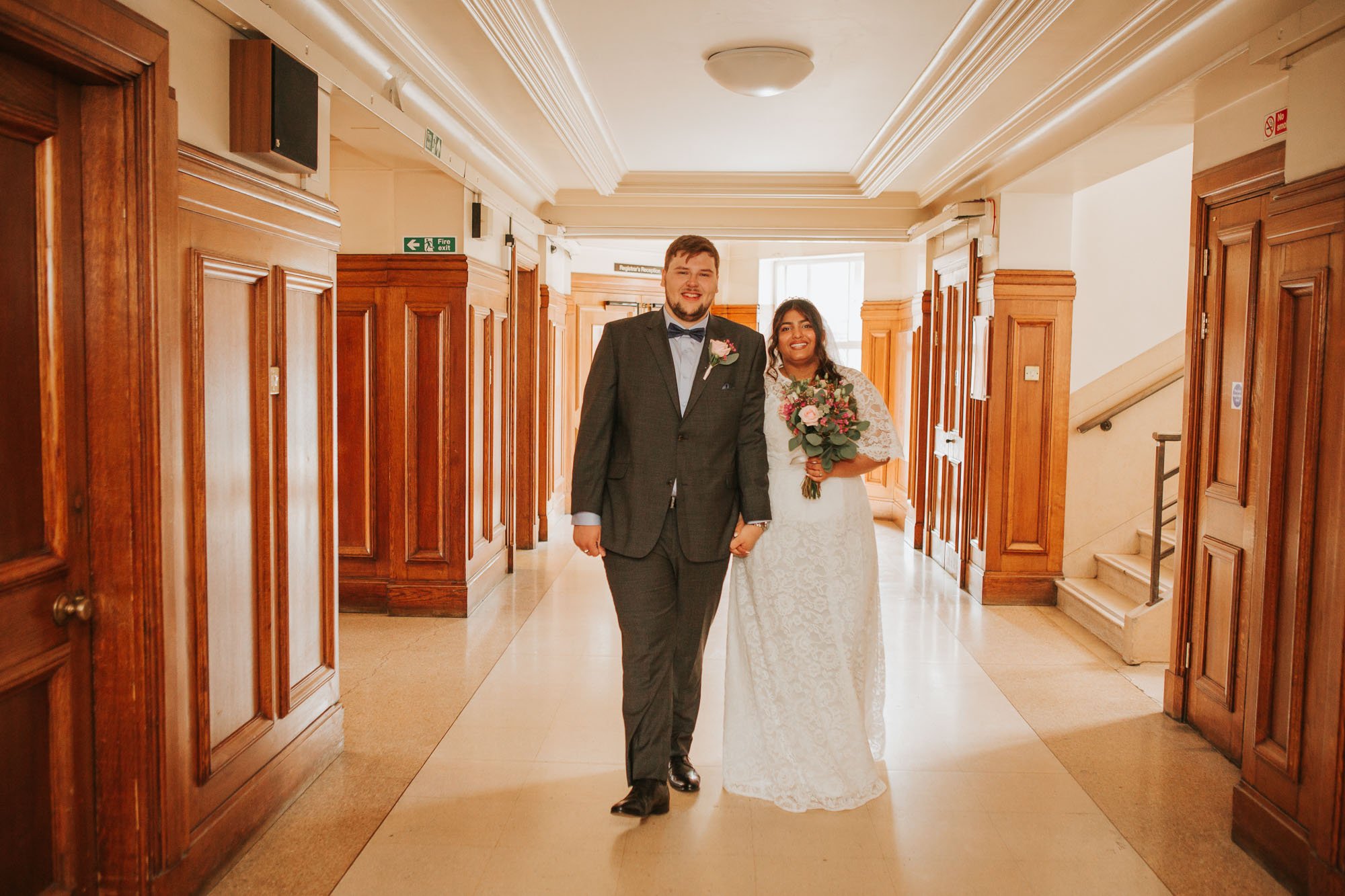  Newly married bride and groom walking along hand in hand down the corridors at Wandsworth Town Hall. 