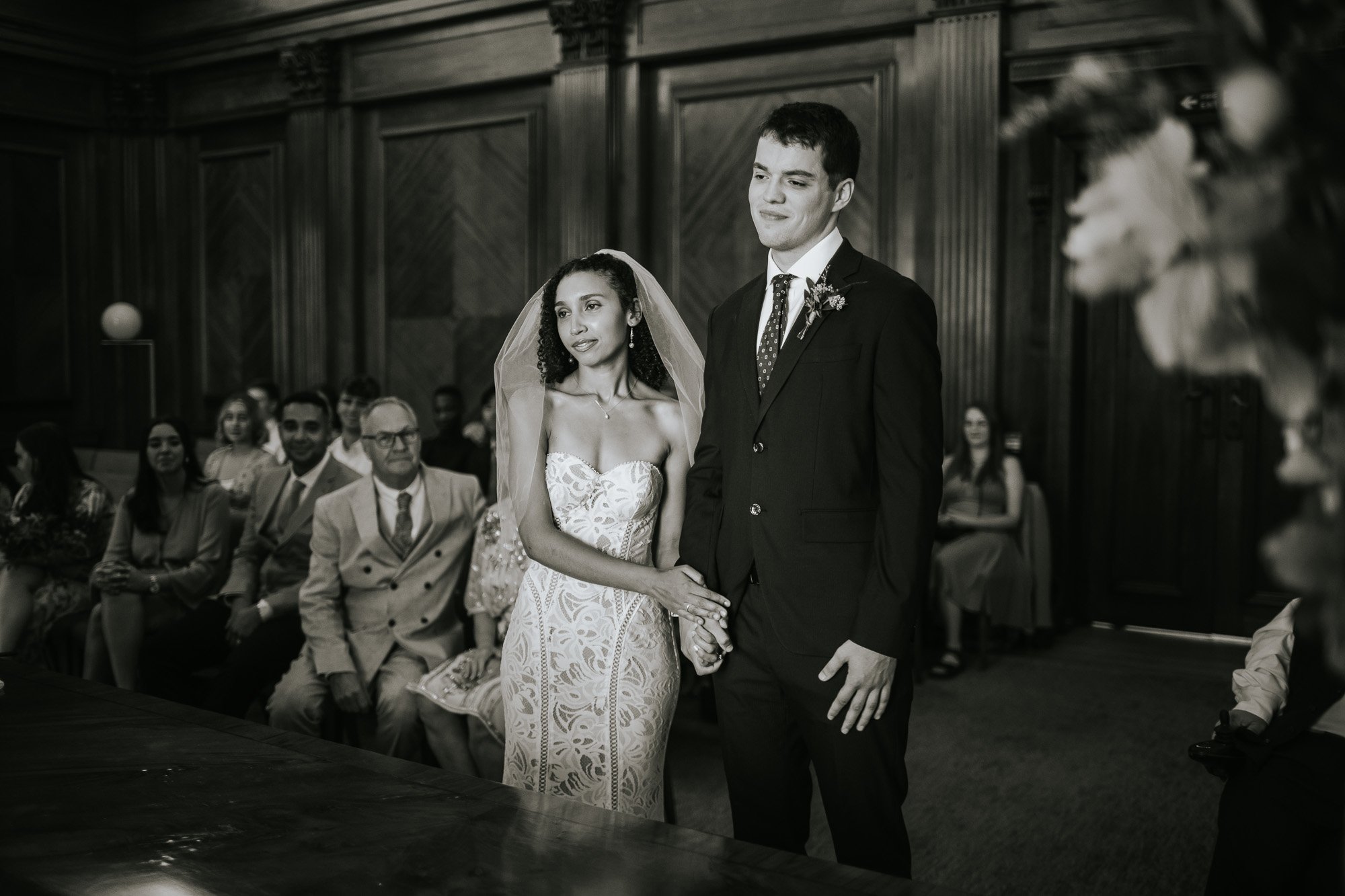  A black and white picture of the bride and groom standing in front of the registrar in the Westminster room at Marylebone town hall in Marylebone, London. 