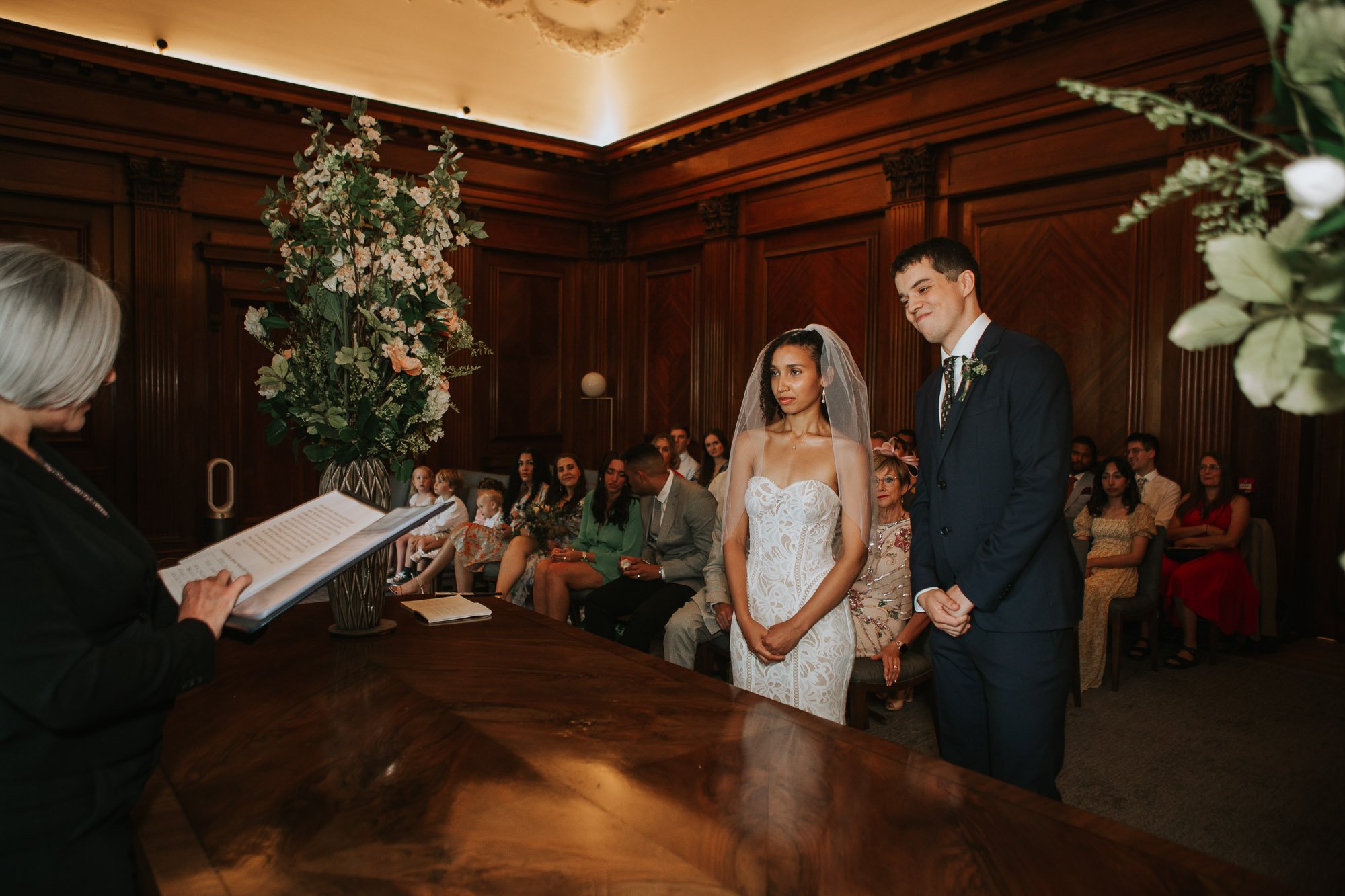  The bride and groom standing in front of the registrar in the Westminster room at Marylebone town hall in Marylebone, London. 