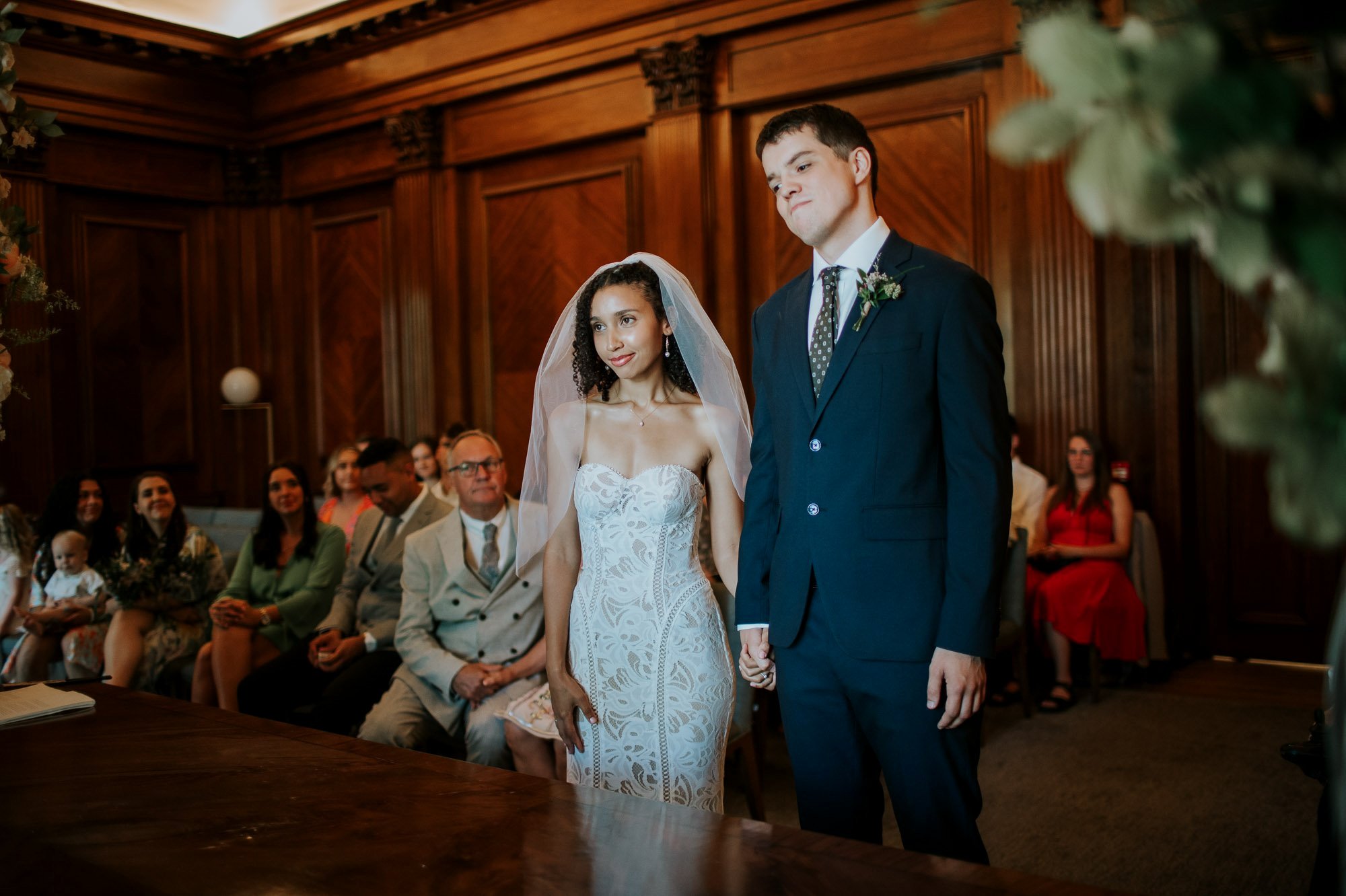  The bride and groom holding hands and standing in front of the registrar in the Westminster room at Marylebone town hall in Marylebone, London. 