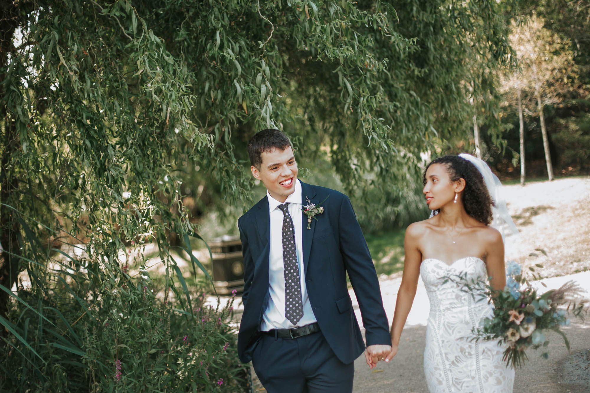  Bride and Groom walking hand in hand along a pathway in Regents Park in London. 