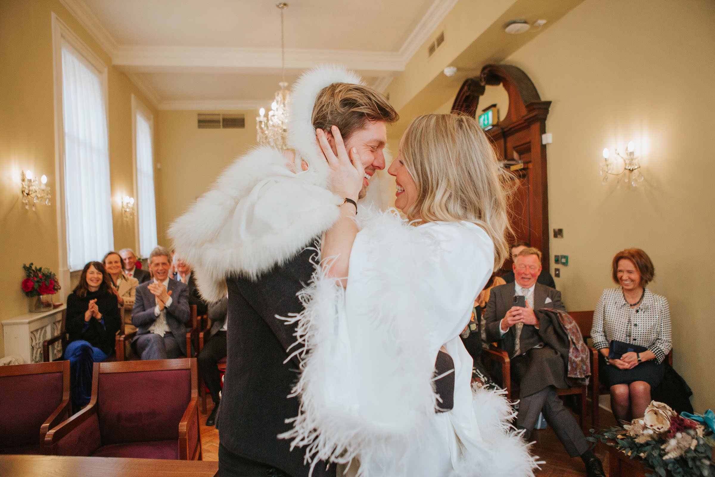  Lizzie and Max about to kiss in their wedding ceremony in front of their friends and family in The Byron Room at Chelsea Old Town Hall. 