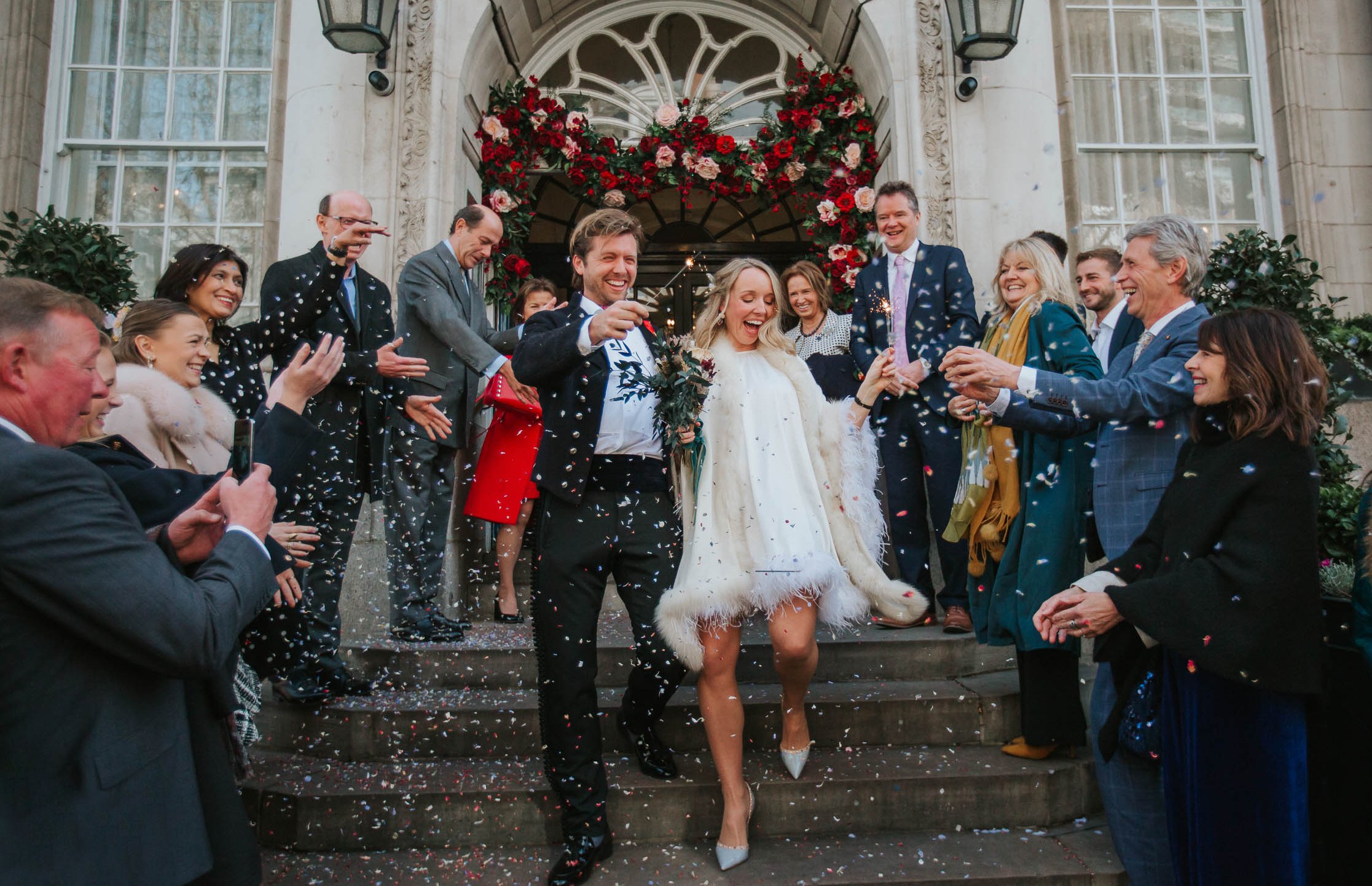  Newly married bride and groom walking down the steps at Chelsea Old Town Hall while their guests shower them with confetti. 