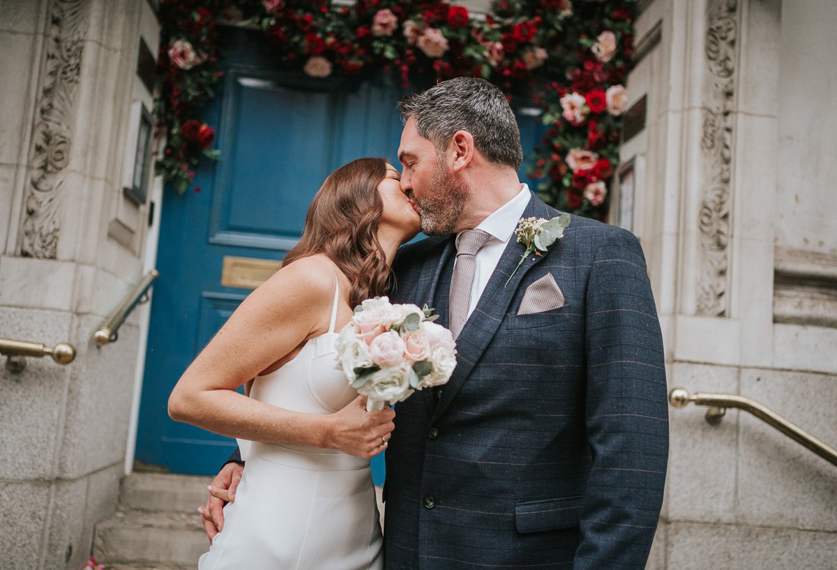  A bride and groom kissing on the steps outside Chelsea Old Town Hall. 