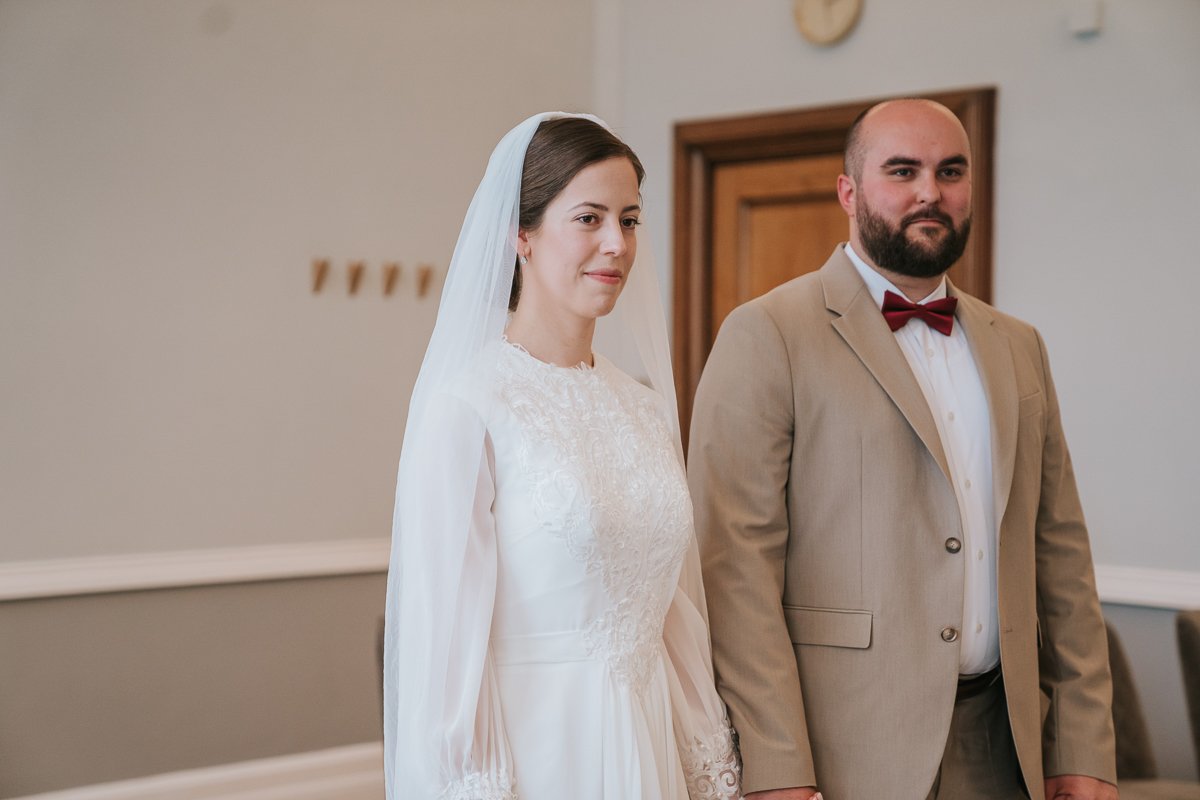  Edina and Zsolt, the bride and groom, stand next to each other in the wedding ceremony room at Islington Town Hall. 