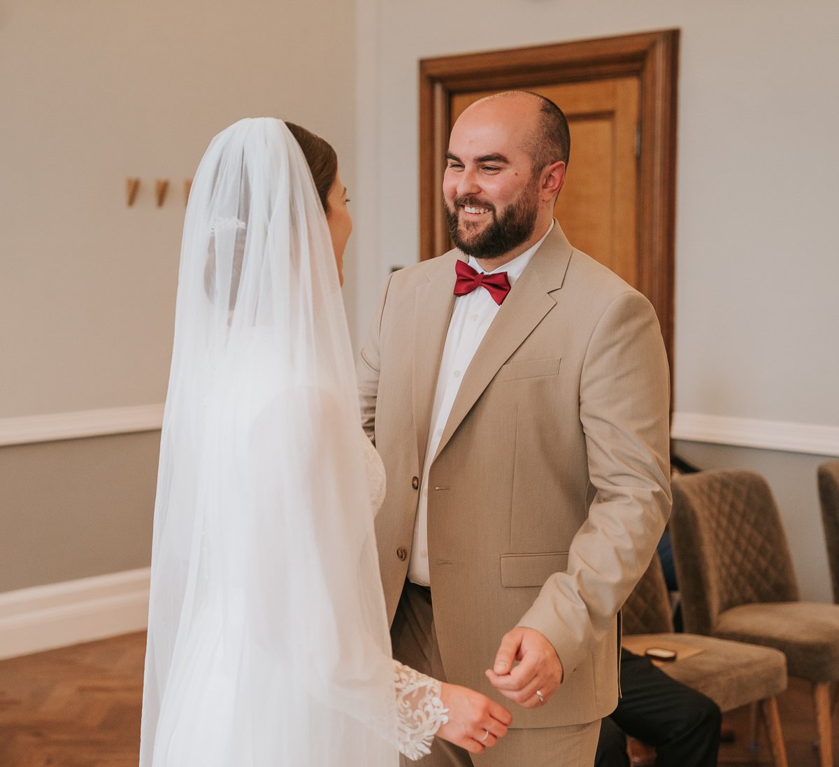  Edina and Zsolt, the bride and groom, face each other smiling as they get married in the wedding ceremony room at Islington Town Hall. 