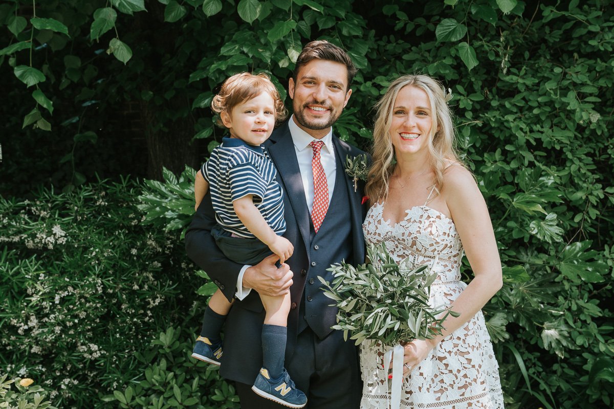  Bride and Groom and their baby son posing for photographs in the garden of Southwark Register Office. 