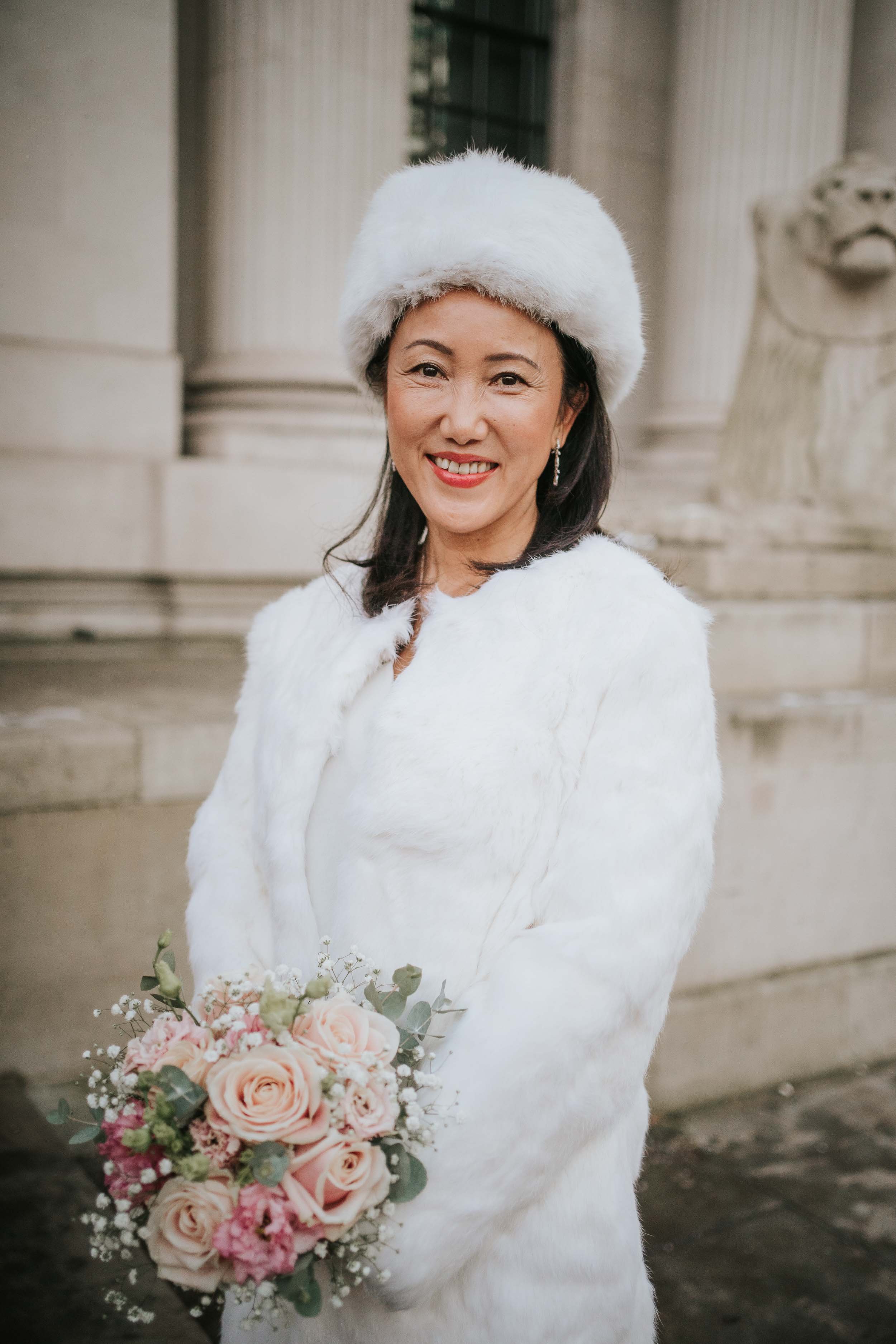  Bride posing outside Old Marylebone Town Hall and looking into the camera. She holds a bouquet of wedding flowers. 
