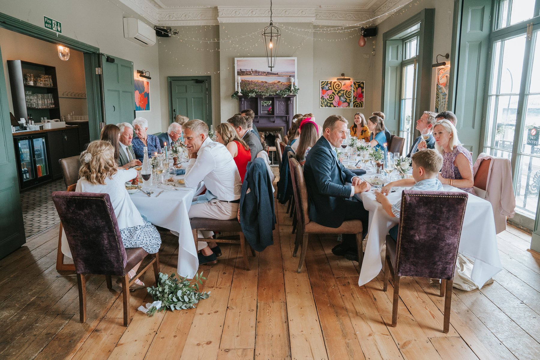  Side view of Bride and Groom and guests sitting at the dining table in The Melrose Room at The Bulls Head. 