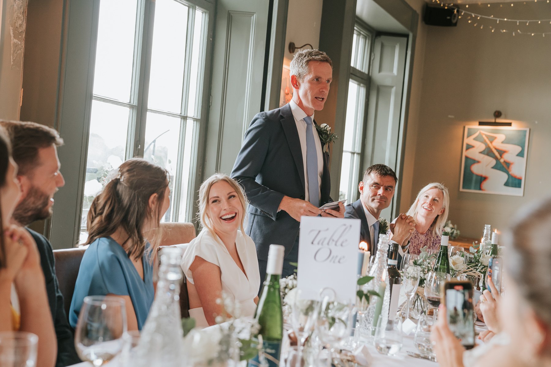  Groom stands at the dining table in The Melrose Room at The Bulls Head and gives speech. 