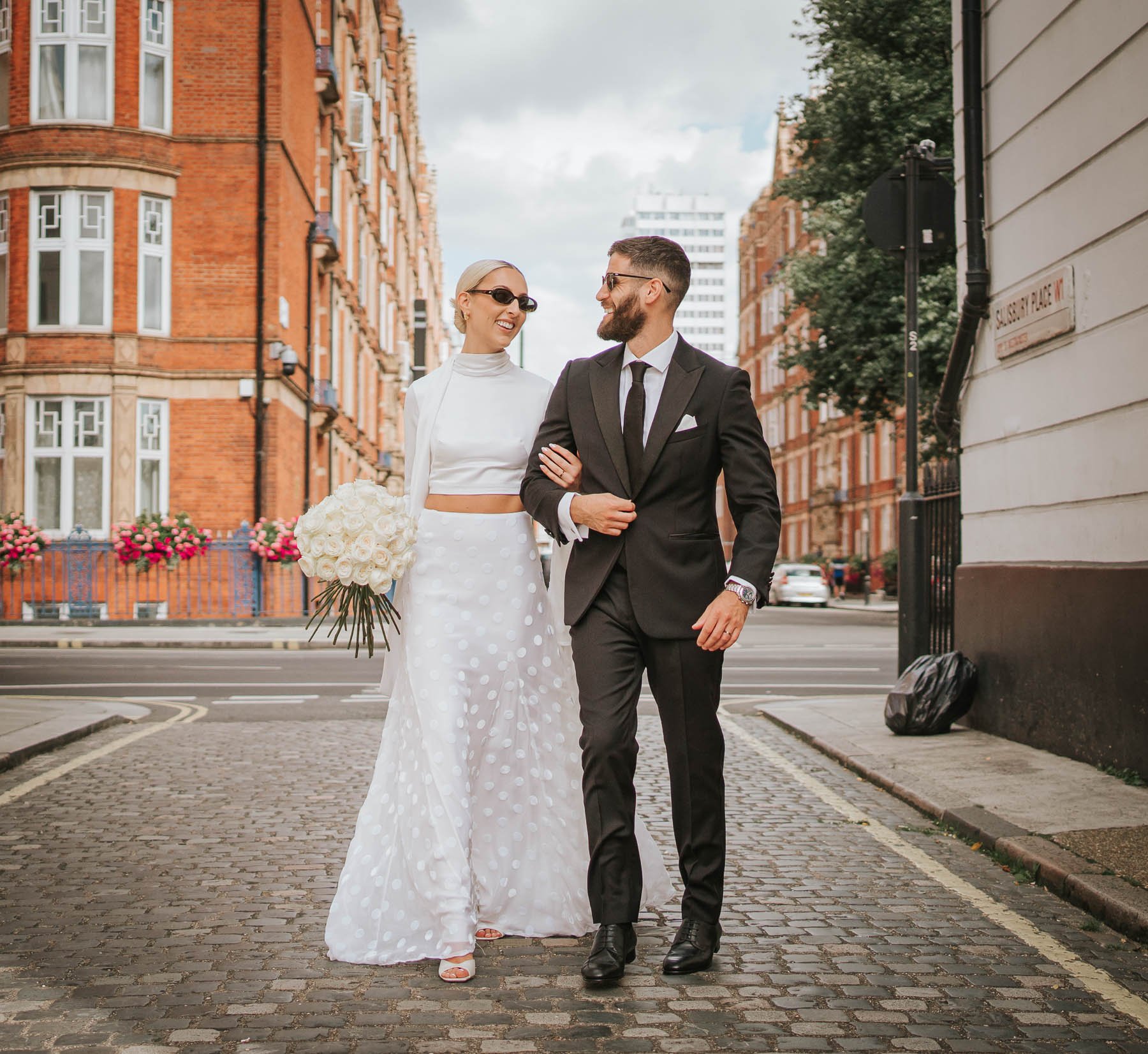  Bride and groom walk arm in arm down street near Marylebone Town Hall. 