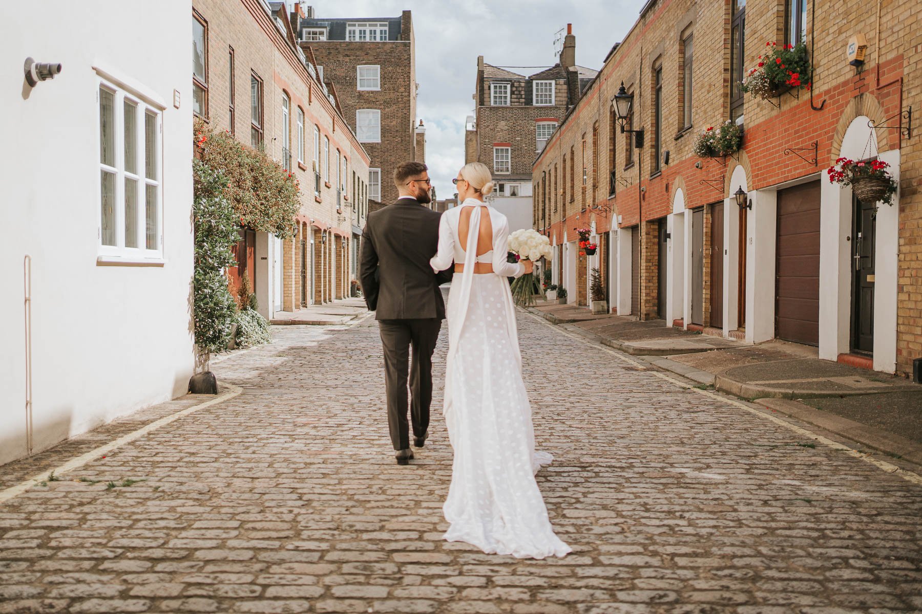  Bride and groom walk away from photographer down cobbled street behind Marylebone Town Hall.  