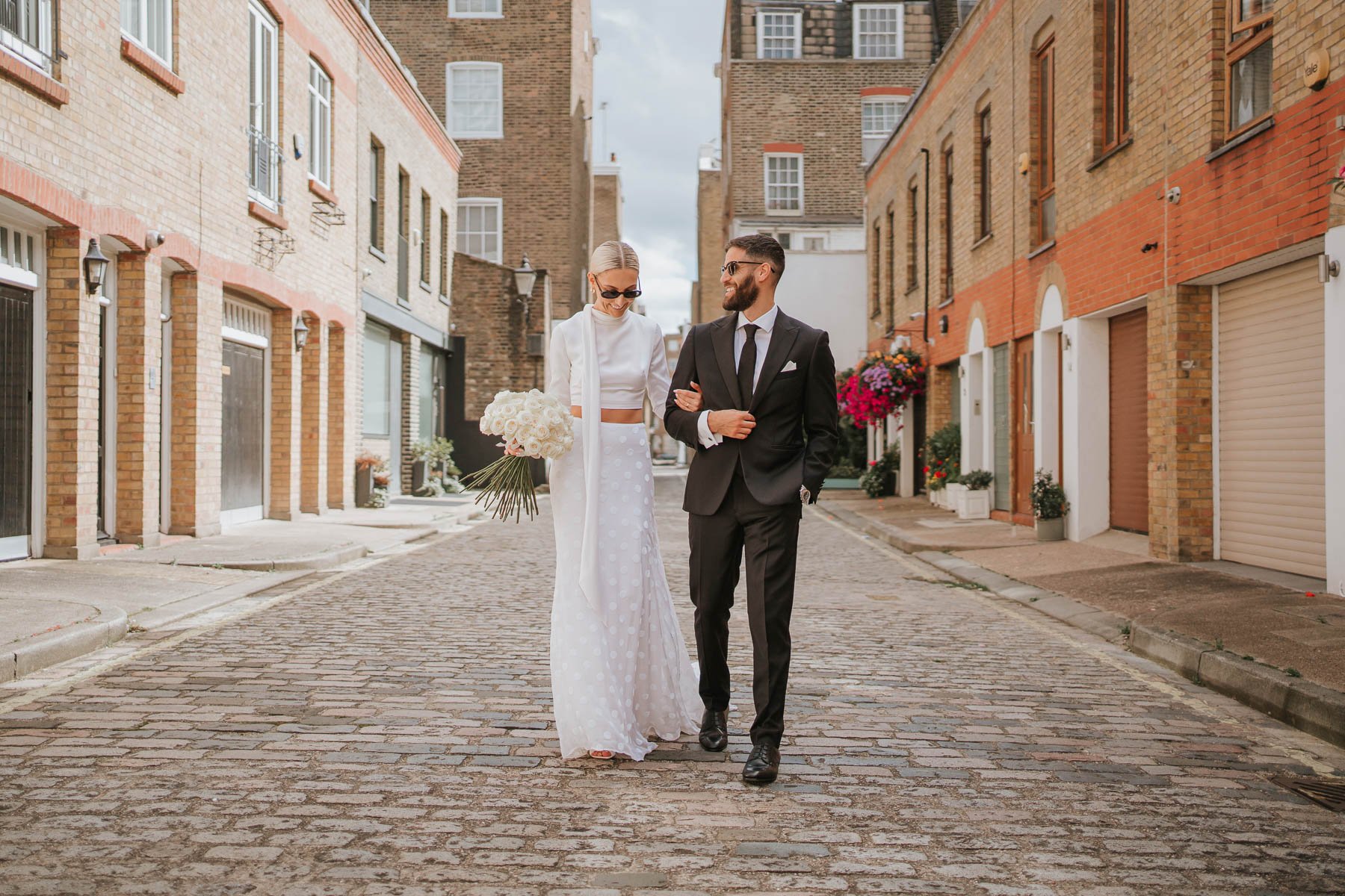  Bride and groom walk towards photographer down cobbled street behind Marylebone Town Hall.  