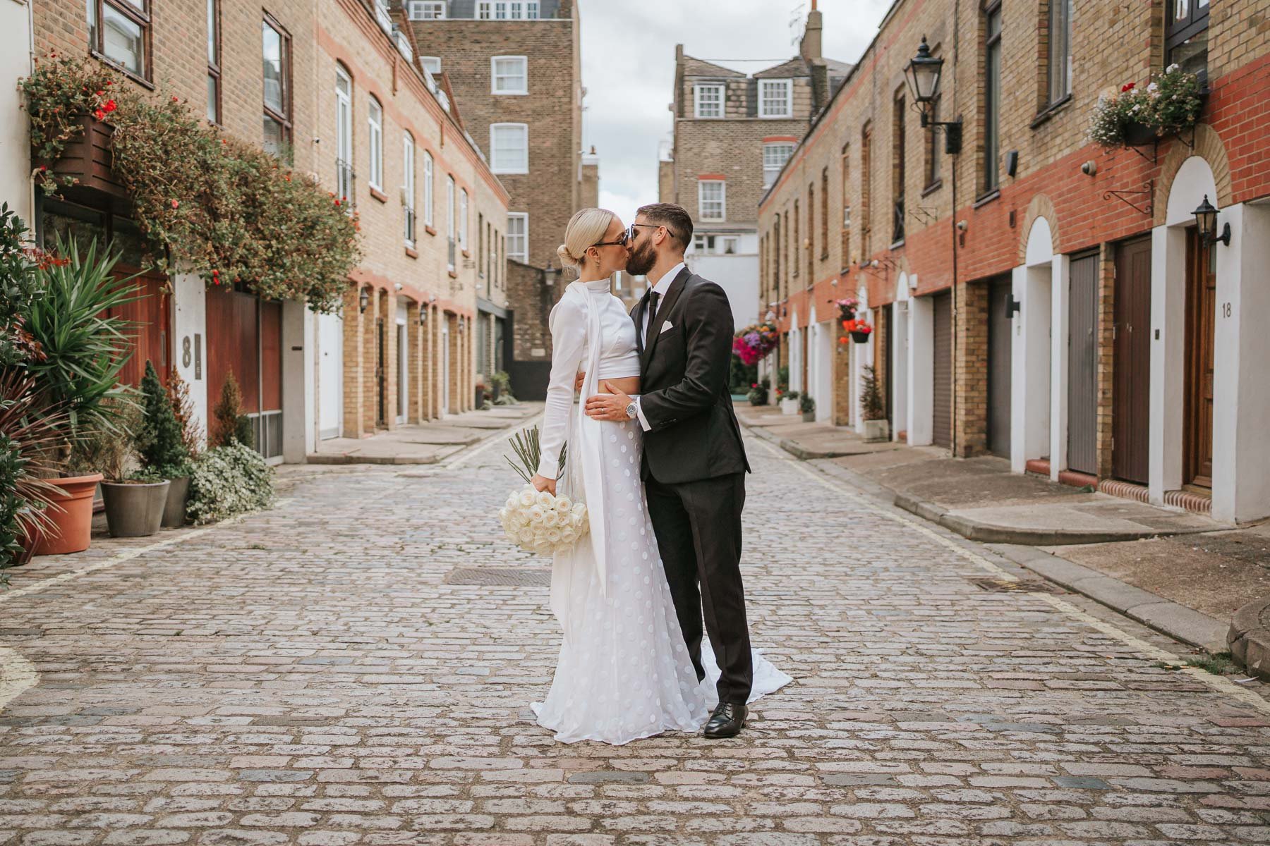  Bride and groom kiss in middle of cobbled street behind Marylebone Town Hall. 