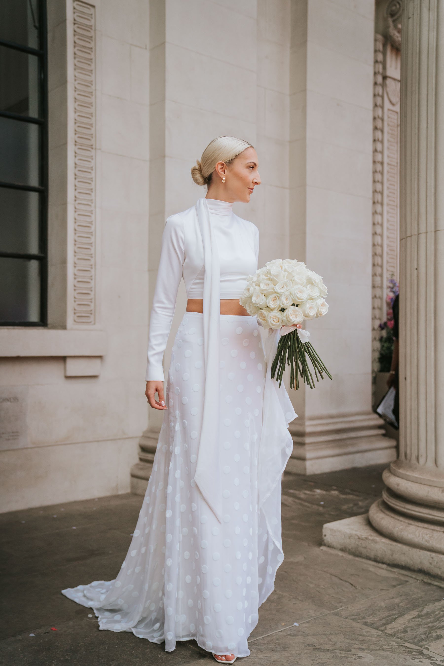  Bride Abbie poses for a photograph holding her bouquet of flowers between the columns outside the old marylebone town hall. 